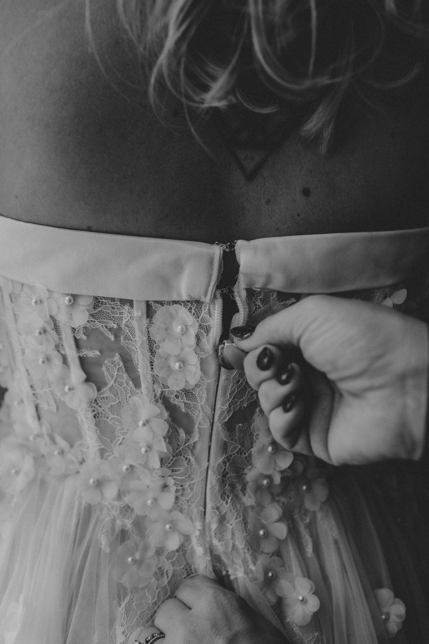 Close-up view of someone fastening delicate buttons on the back of an ornate white wedding dress.