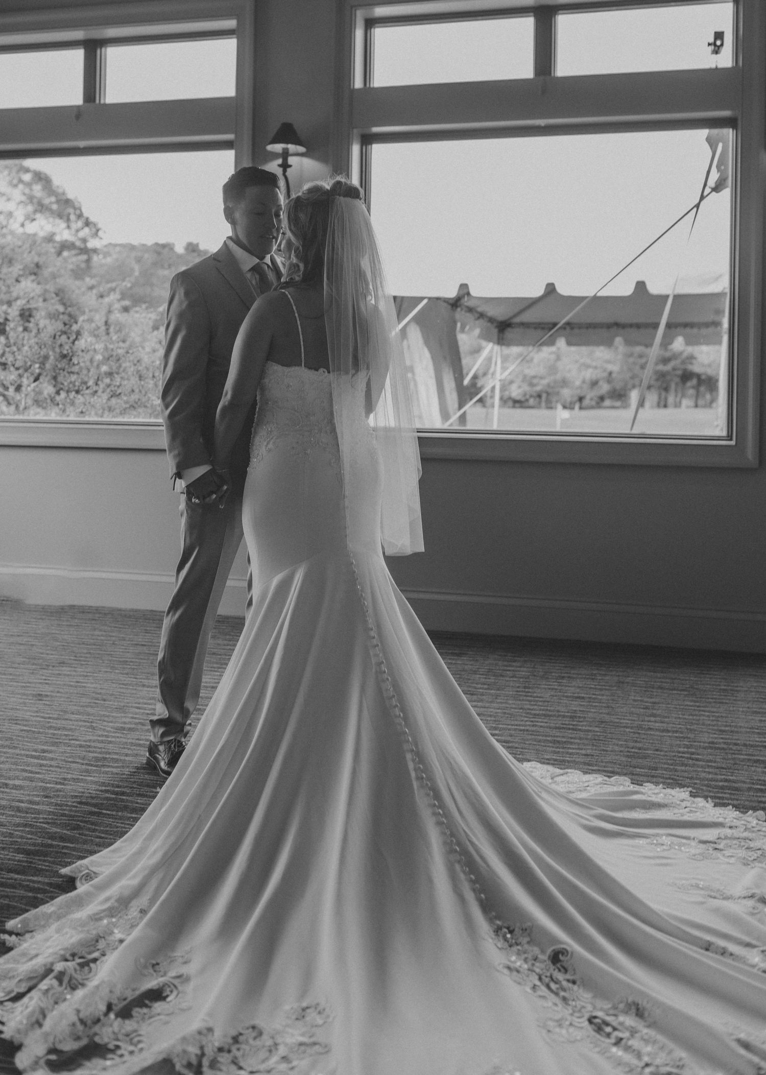A wedding dress train spreads elegantly across a floor while being adjusted in black and white photography.