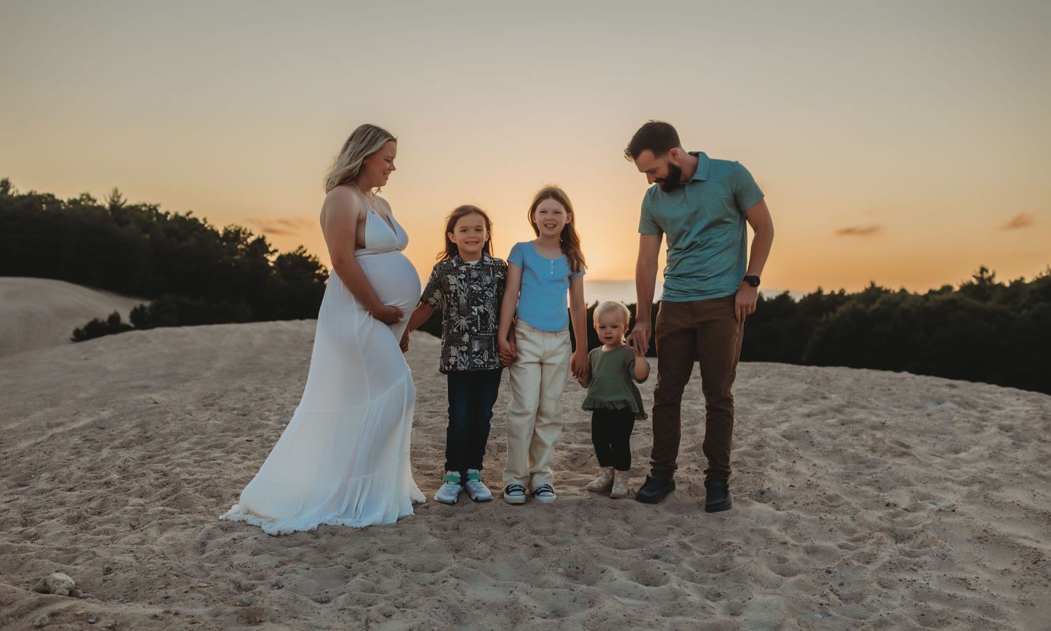 Family enjoying sunset on a sandy beach while taking photos during golden hour.