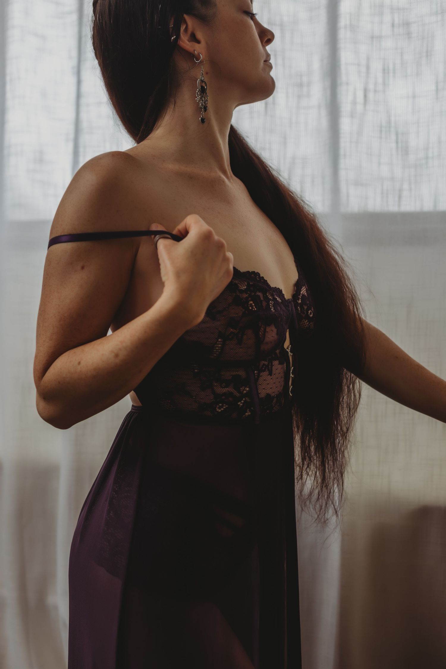 Artistic boudoir photo showing silhouette in black lace lingerie dress against sheer curtain backdrop.