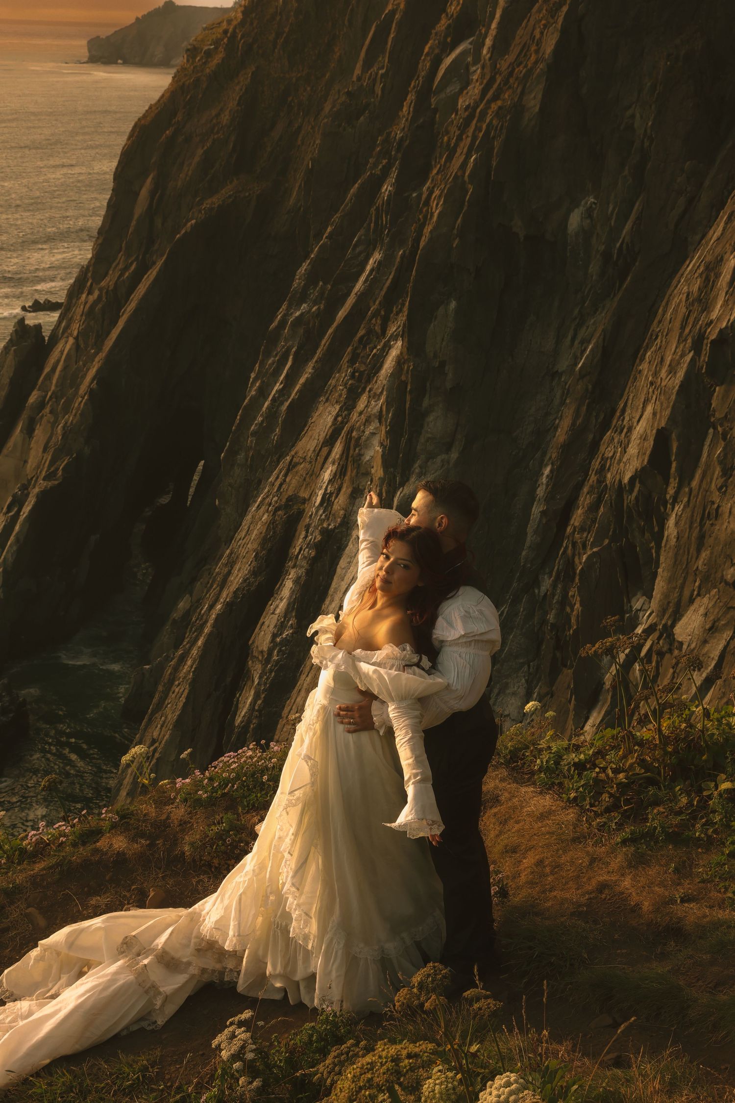 Couple embracing during their Oregon Coast elopement with waves and coastal cliffs behind them
