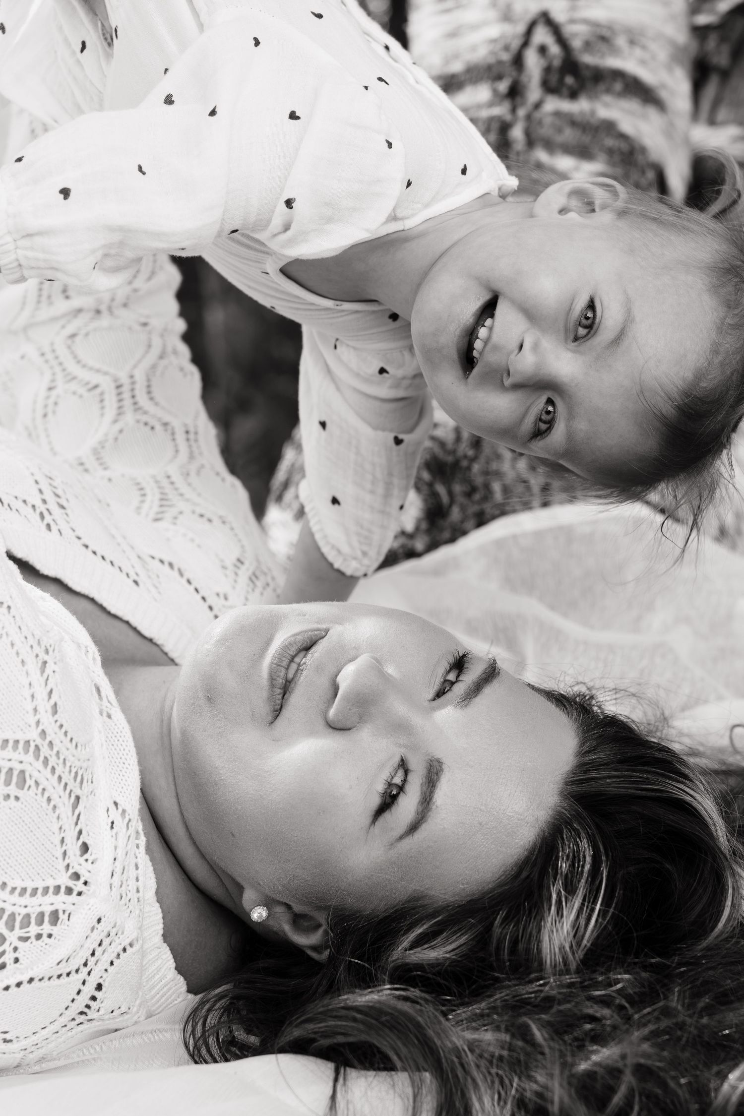 Black and white photo of a smiling mother and daughter in white dresses sharing a joyful moment together.