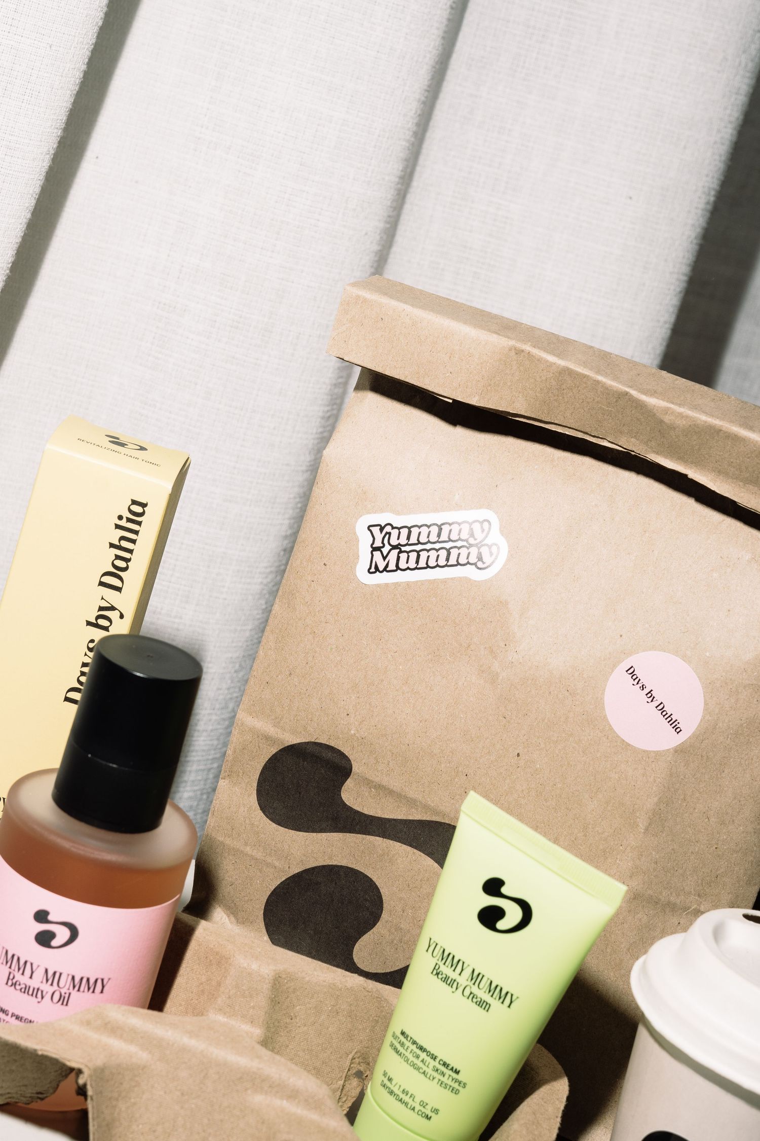Yummy Mummy branded kraft paper bag with tummy oil, body balm, and Days by Dahlia box on wooden background.