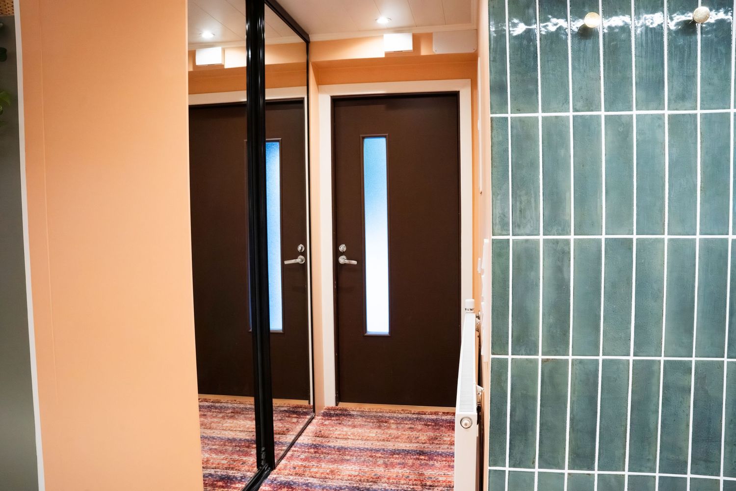 Two dark brown doors with glass panels in a hallway with colorful rug flooring and teal tile wall accent.