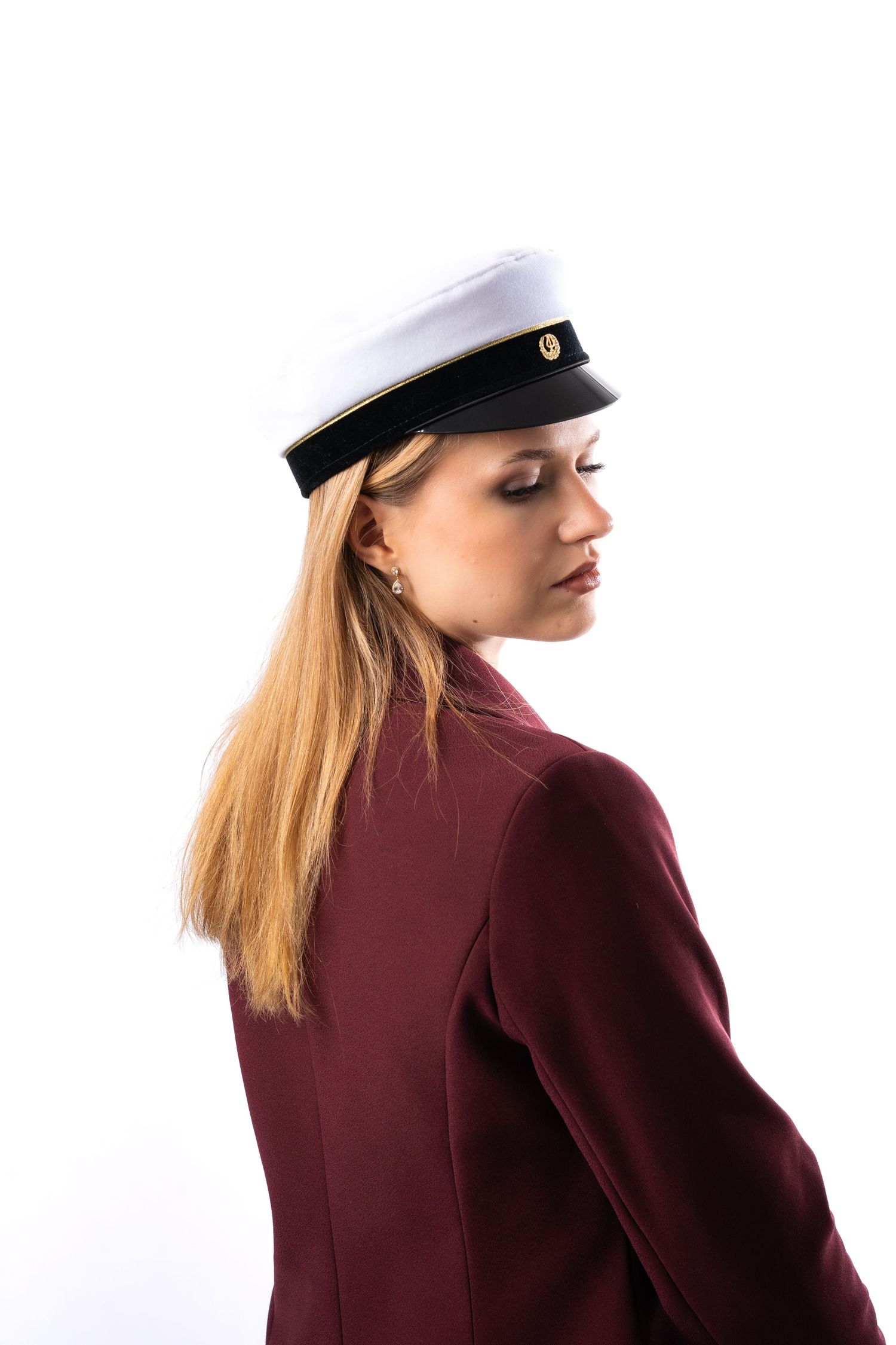 Young blonde woman in burgundy blazer and white naval captain hat poses against white background.