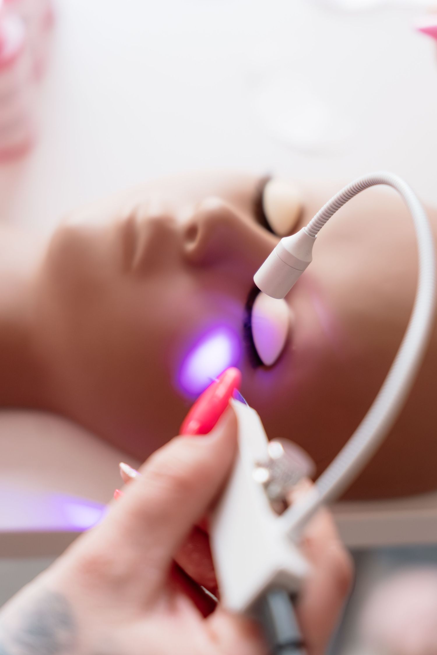Esthetician performing laser skin treatment on woman's face with purple light device.