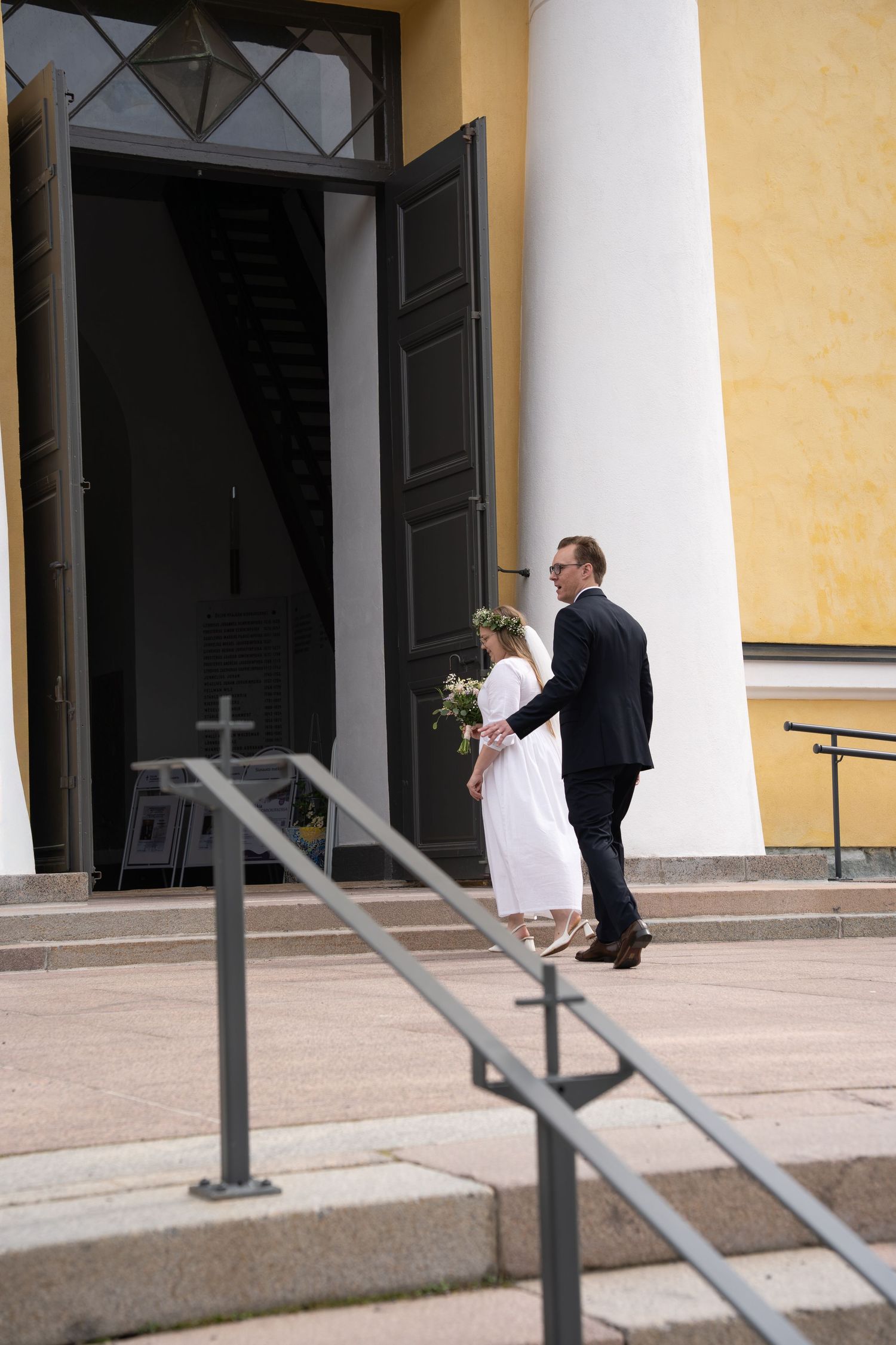 Bride and groom entering a yellow church with large black doors on their wedding day.
