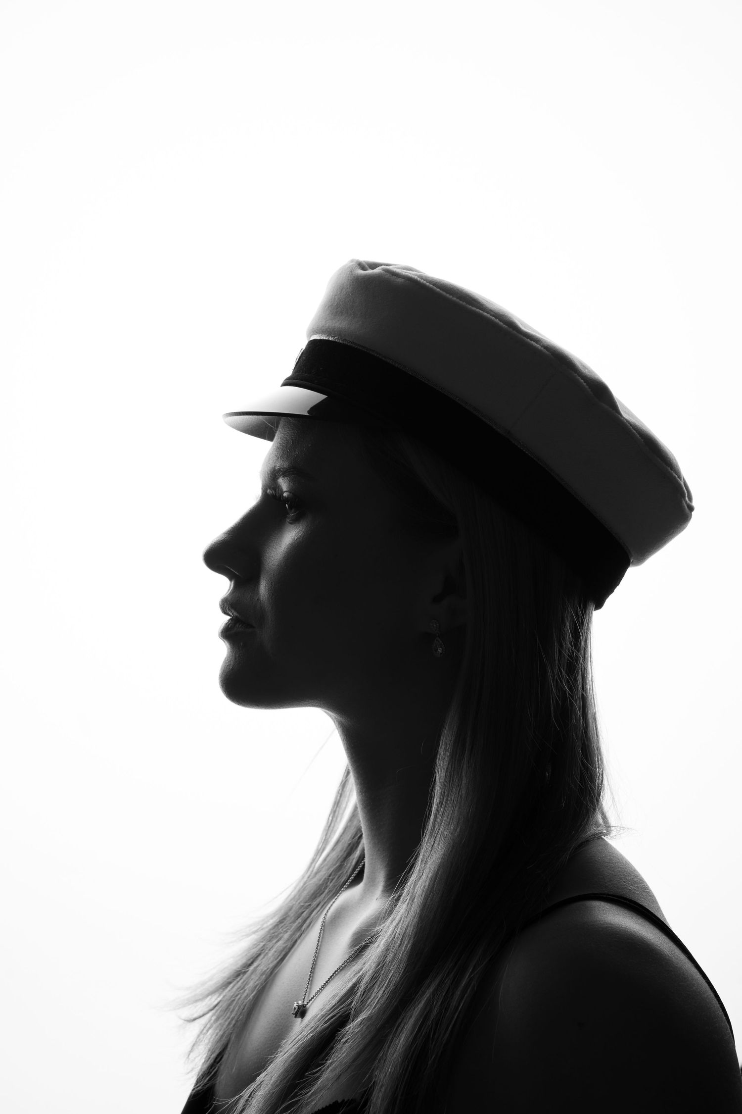 Black and white profile portrait of a woman wearing a captain's hat with long blonde hair against white background.