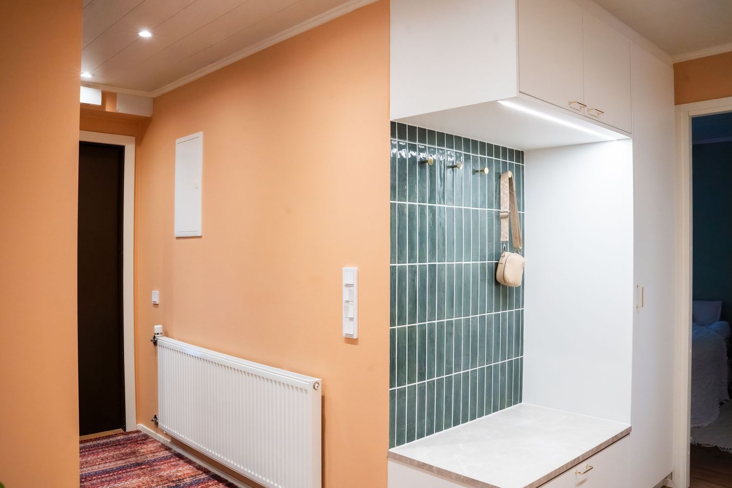 Modern entryway with orange walls, green tile accent wall, white built-in storage, and radiator heating unit.