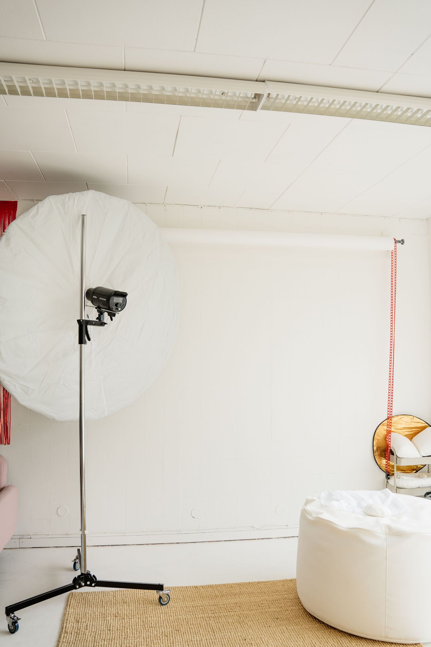 Professional photo studio with large circular softbox light, white backdrop, and white ottoman on natural rug.