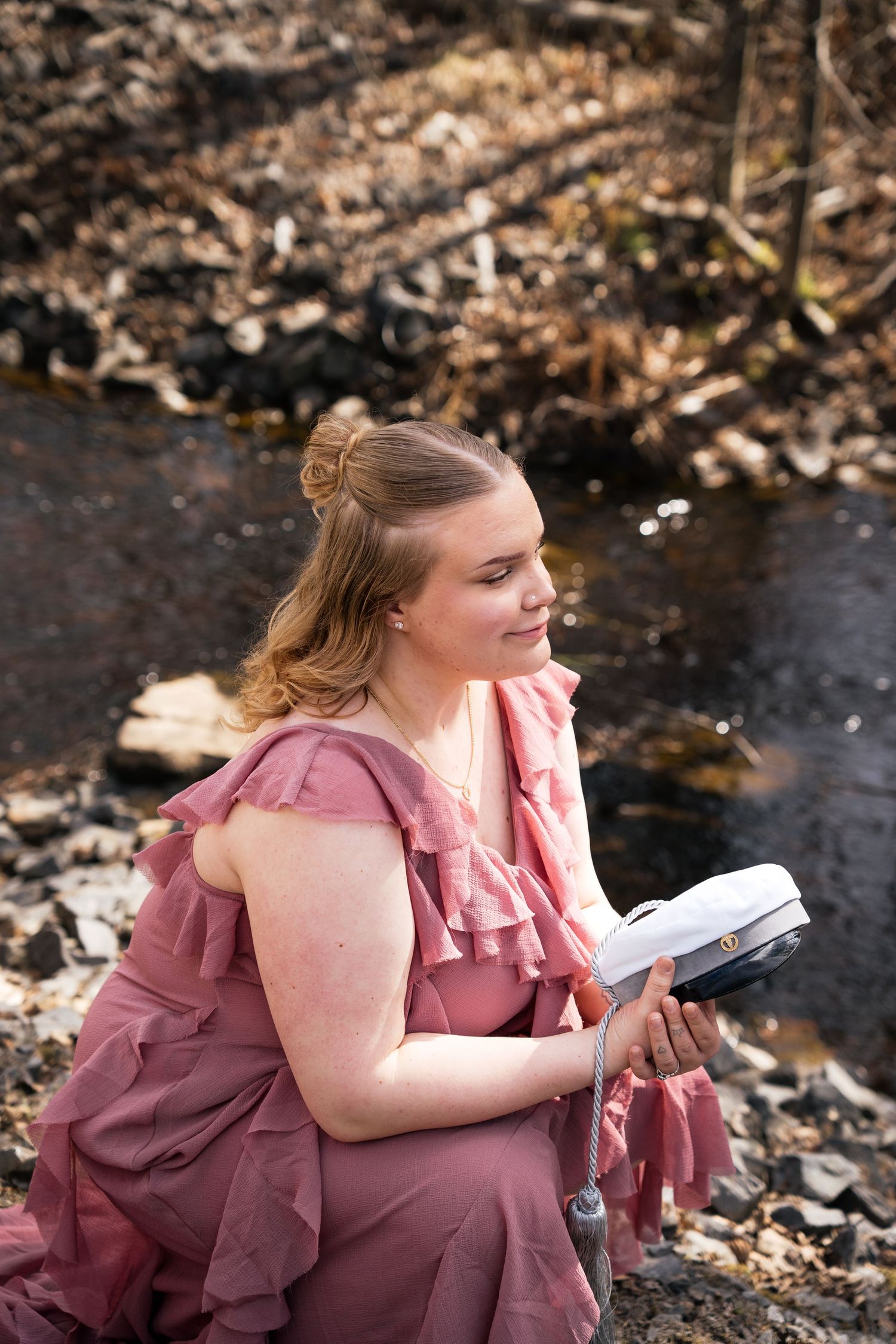 Young woman in pink ruffled dress reading a book by a woodland stream among autumn leaves.