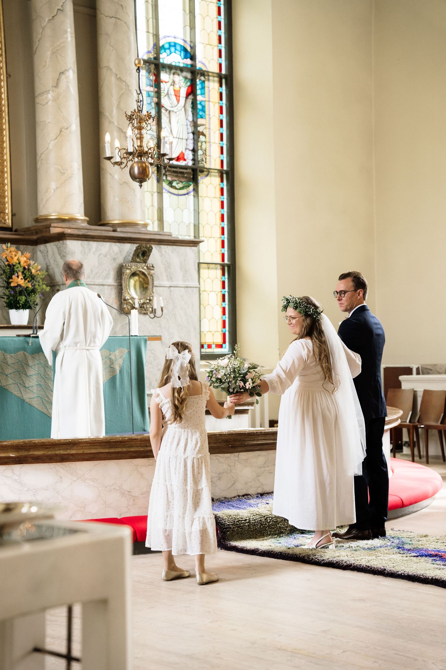 Bride in white dress receives flowers from flower girl at church altar during wedding ceremony.