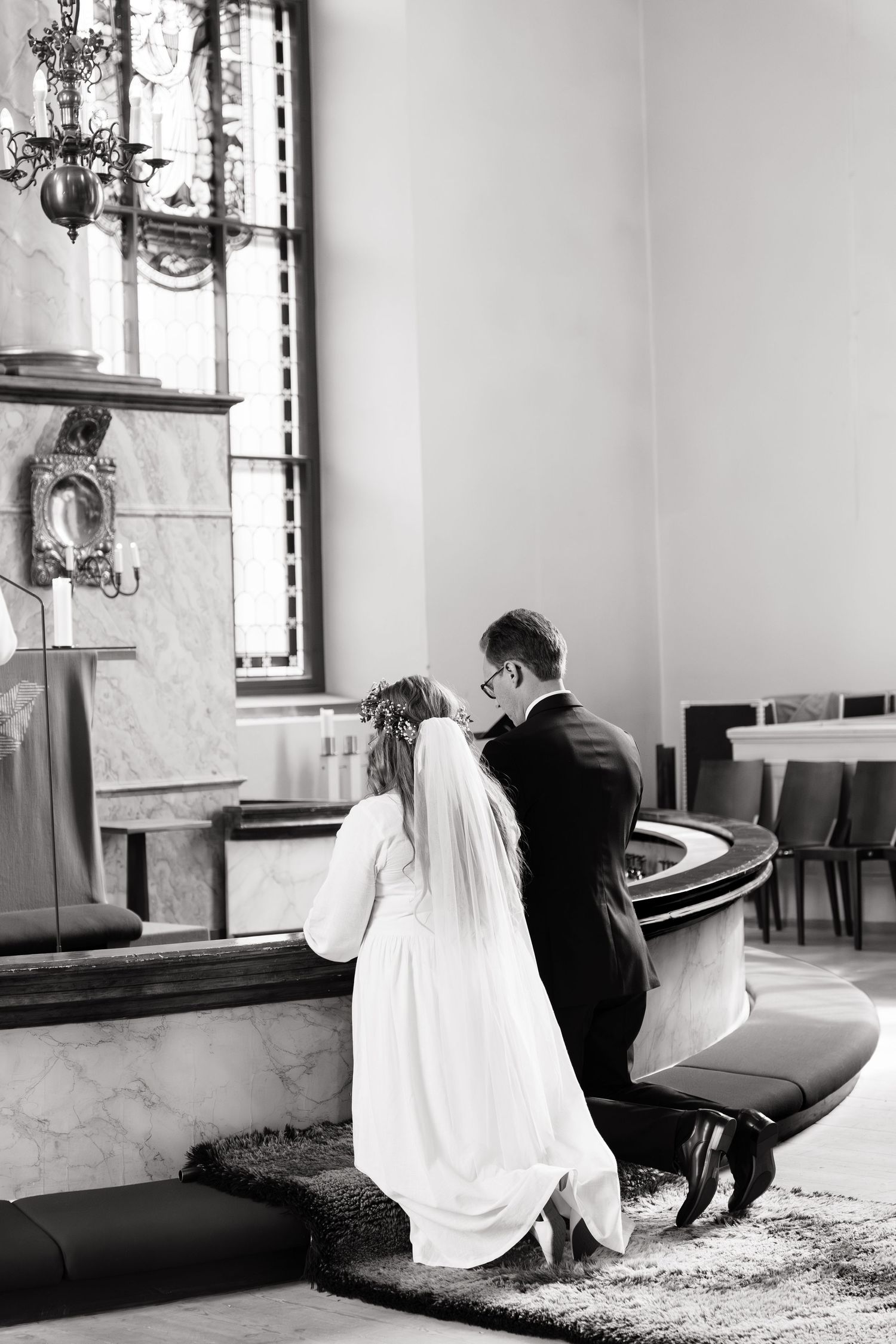 Black and white photo of bride and groom kneeling in prayer at church altar during wedding ceremony.