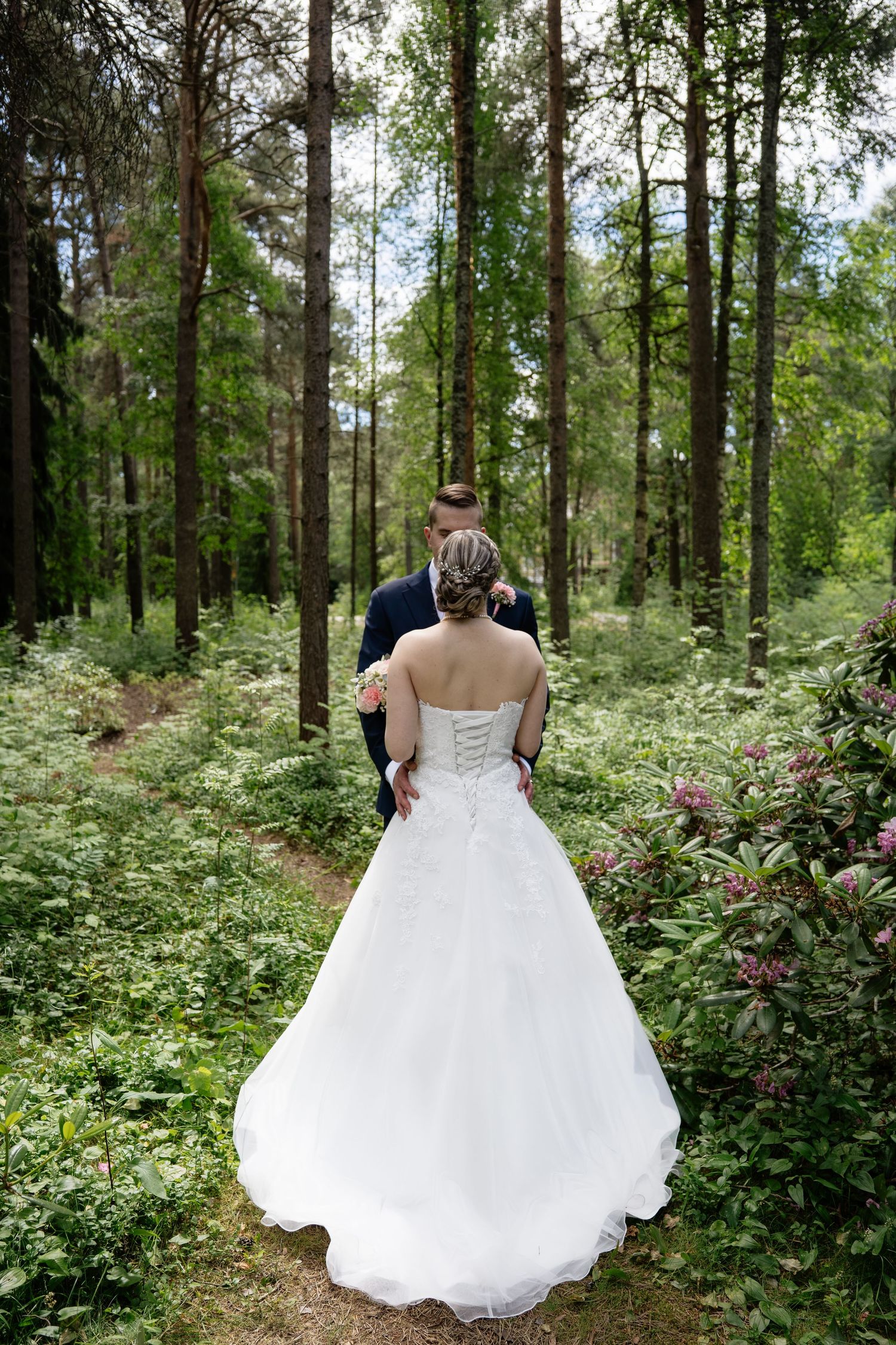 Bride and groom walking hand in hand through a lush green forest on their wedding day.