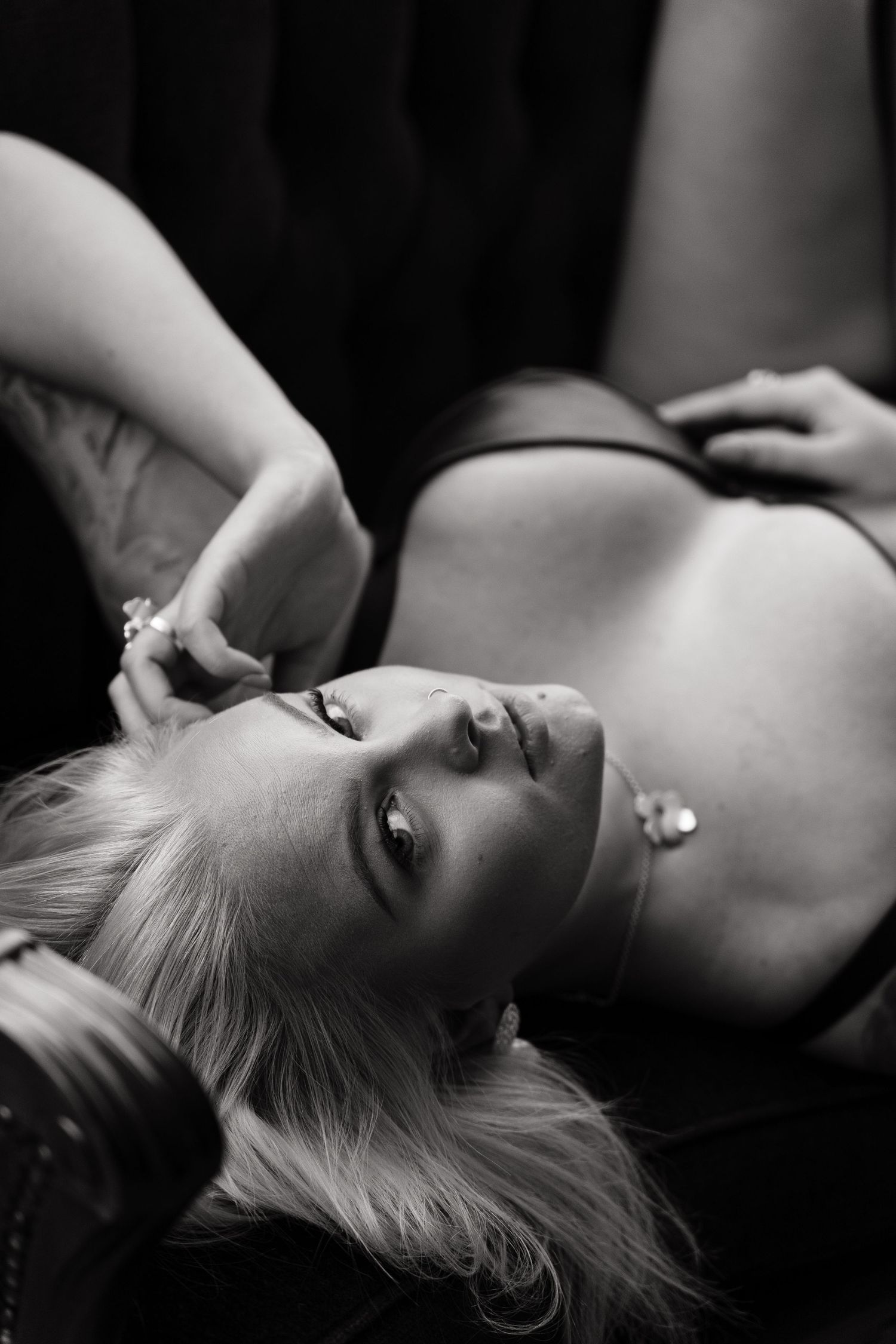 Black and white boudoir photo of a blonde woman lying down wearing lingerie with jewelry accessories.