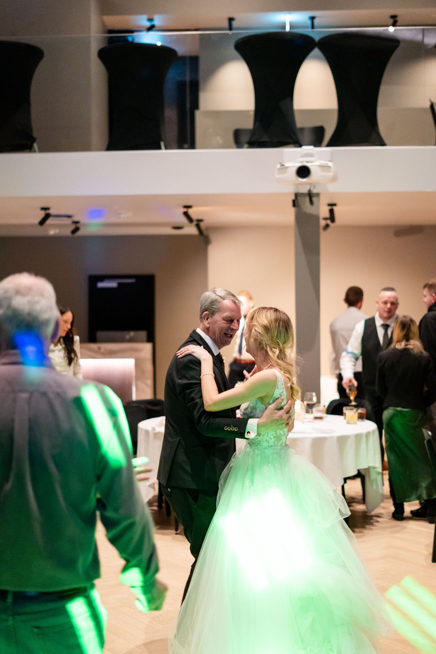 A bride in a green ball gown shares a father-daughter dance at an elegant wedding reception venue.