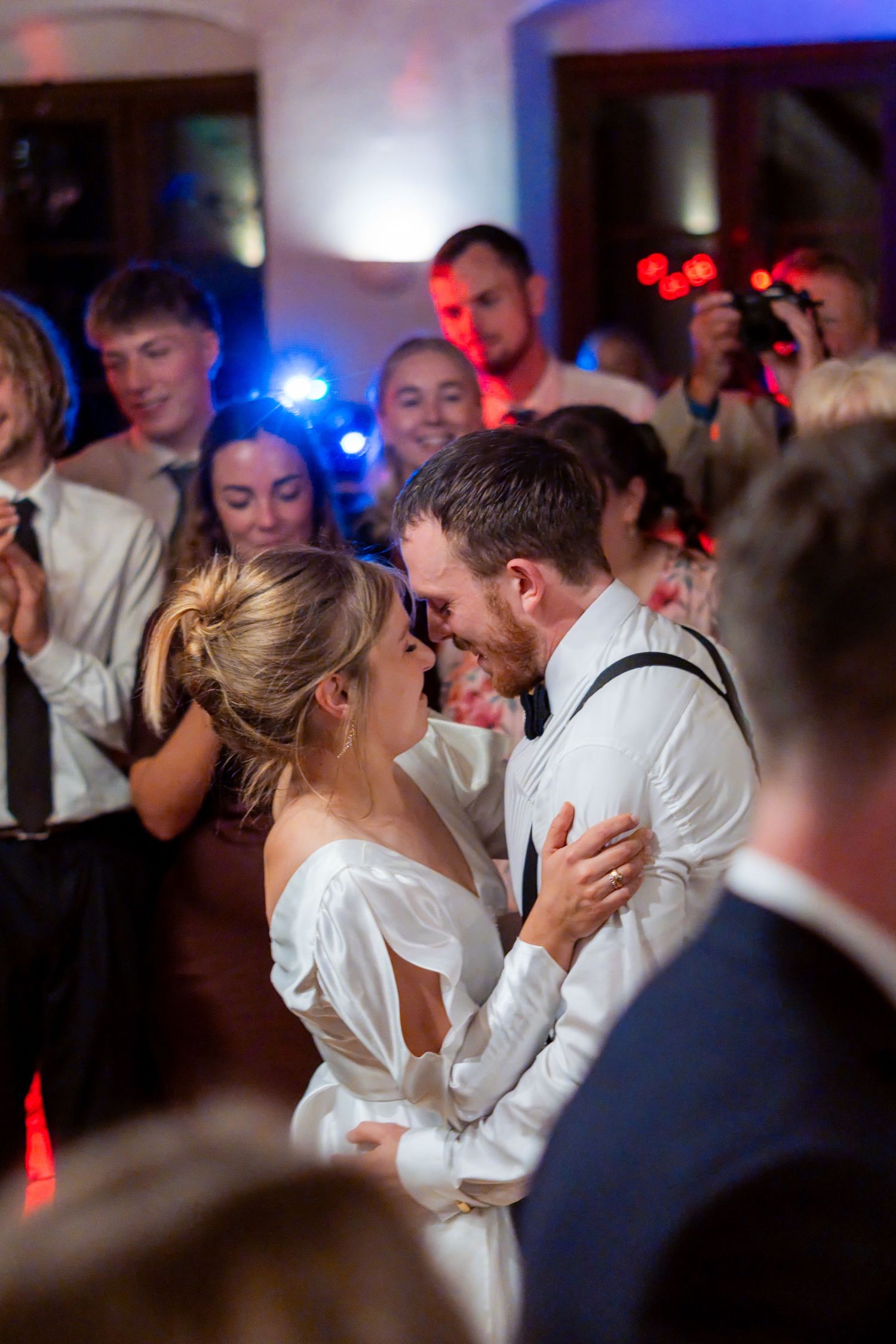 Bride and groom share an intimate first dance surrounded by guests at a romantic wedding reception.