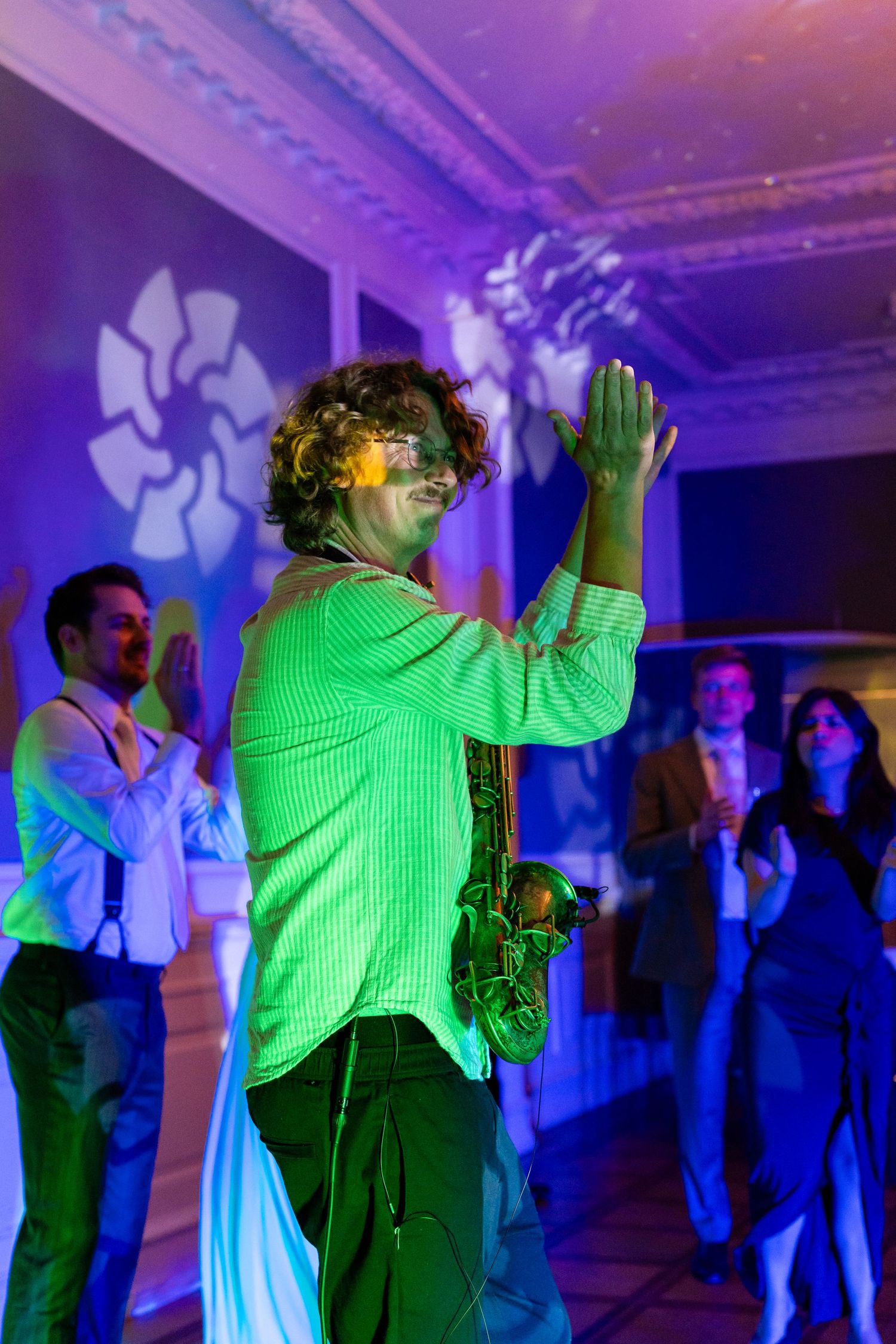 Person in green shirt dancing at a party under colorful purple and blue lights with guests in background.