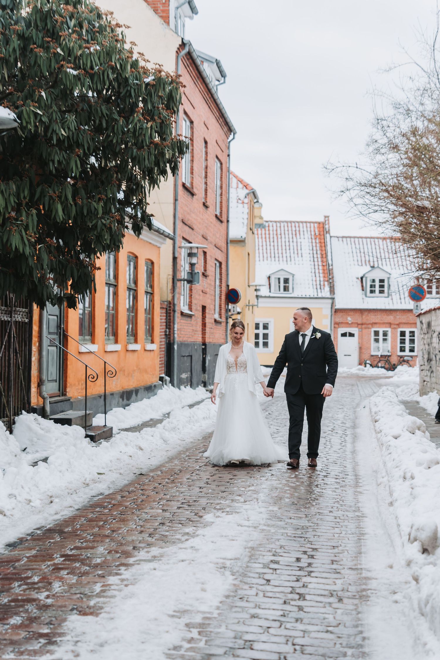 Snow-covered cobblestone street with historic orange buildings and winter wedding scene.