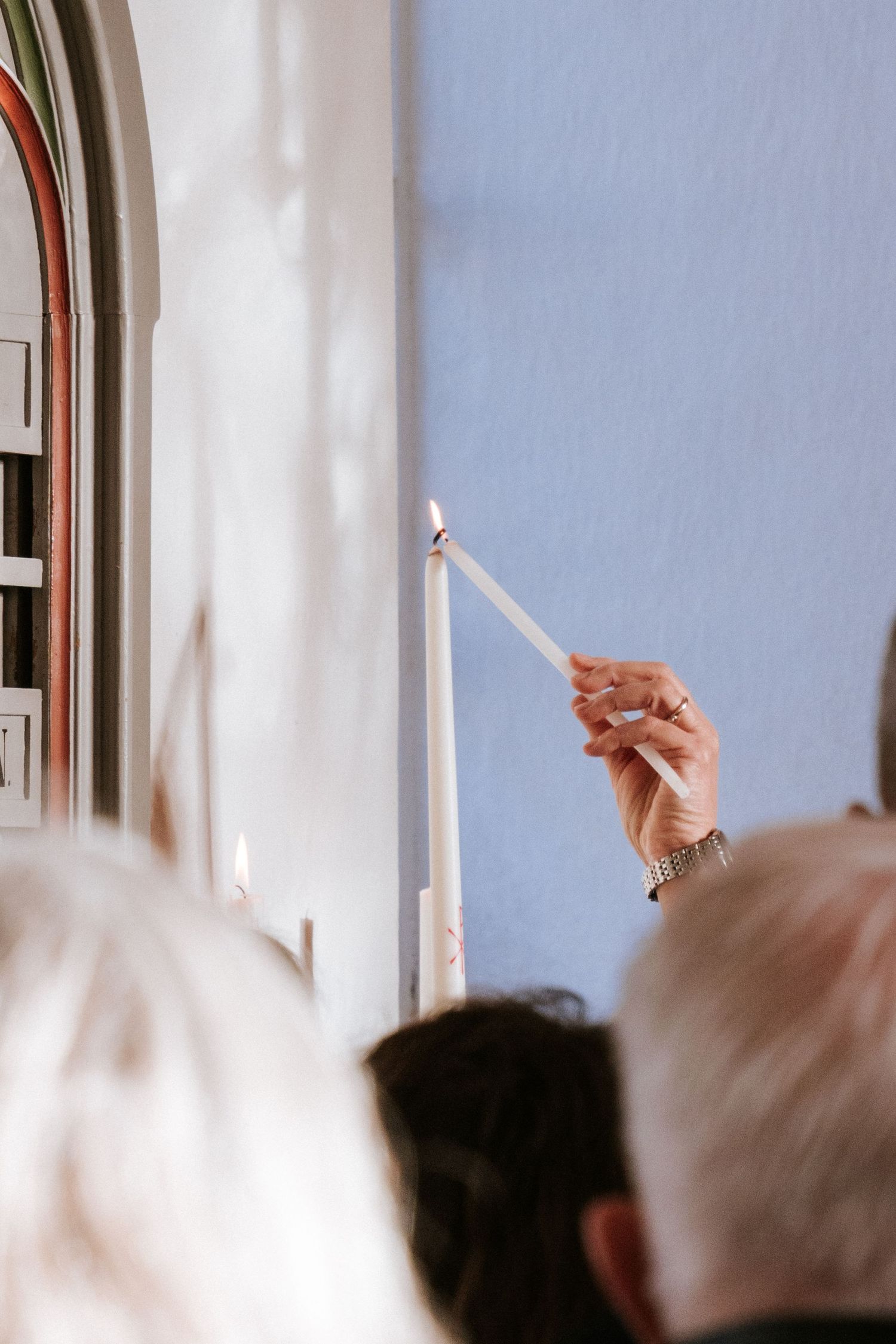 Hands holding lit candles against white walls during a church ceremony.