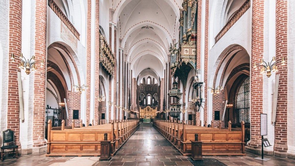 Gothic church interior with white vaulted ceilings and red brick columns creating a dramatic perspective.