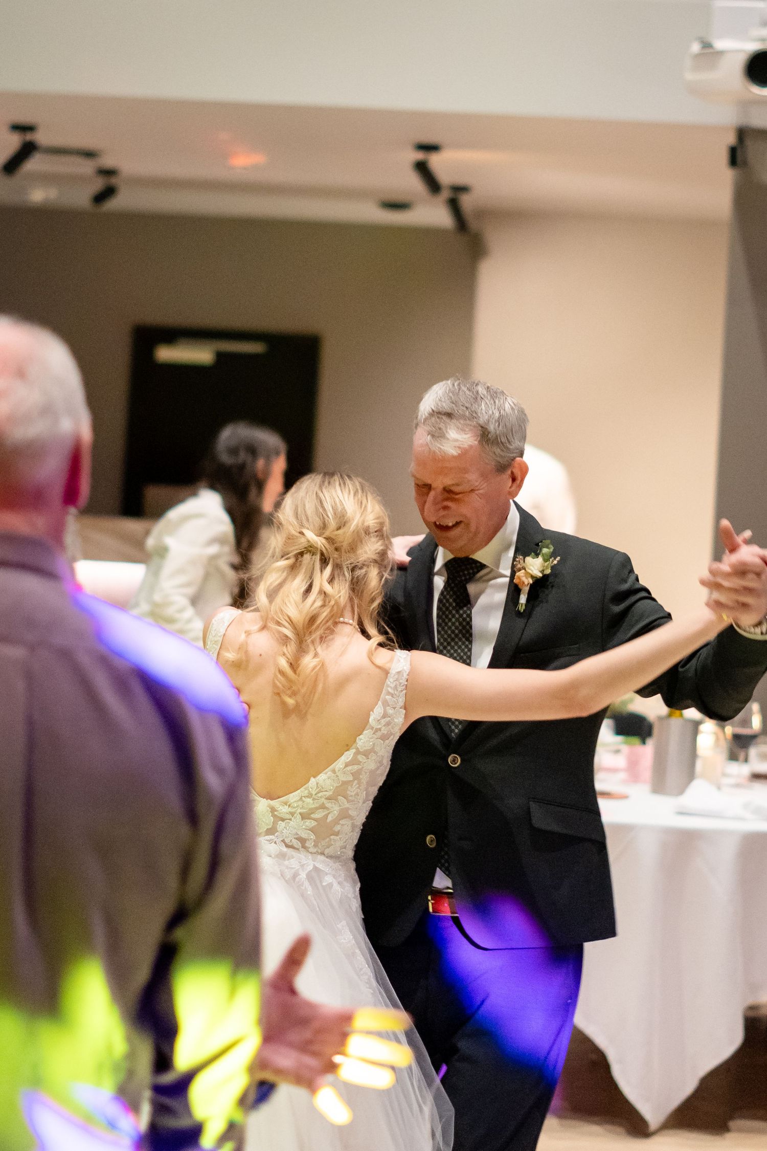 Bride and groom share their first dance at wedding reception, man wearing dark suit with boutonniere.