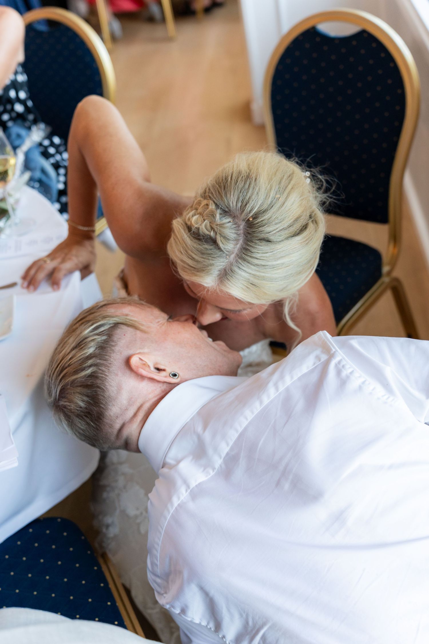 Couple sharing a kiss at a wedding reception, viewed from above, seated at a decorated table.
