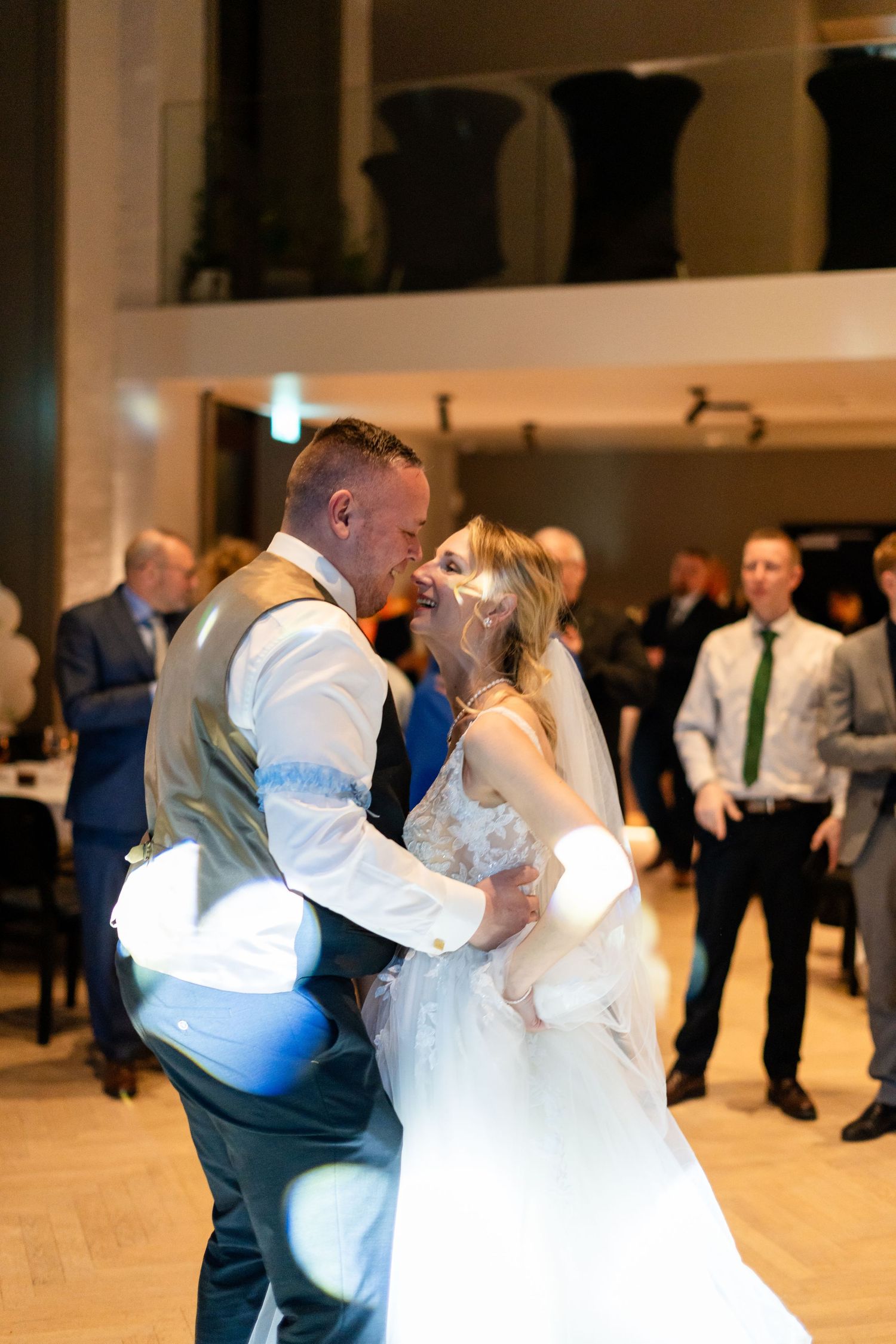 Bride and groom share their first dance at wedding reception, surrounded by guests in elegant venue.
