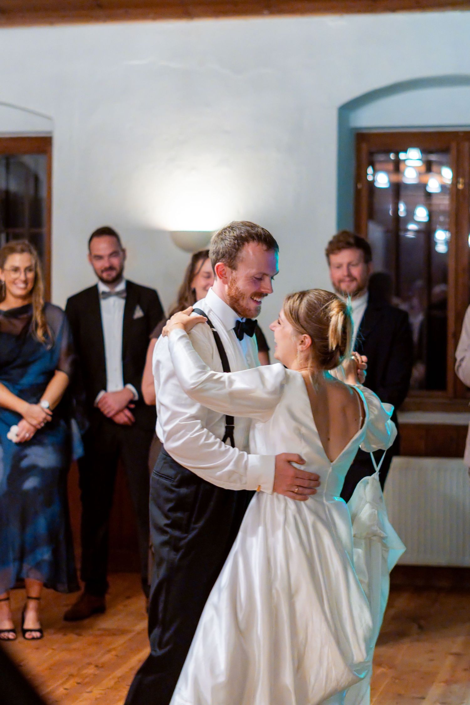 A bride and groom share their first dance at a wedding reception while guests watch in the background.