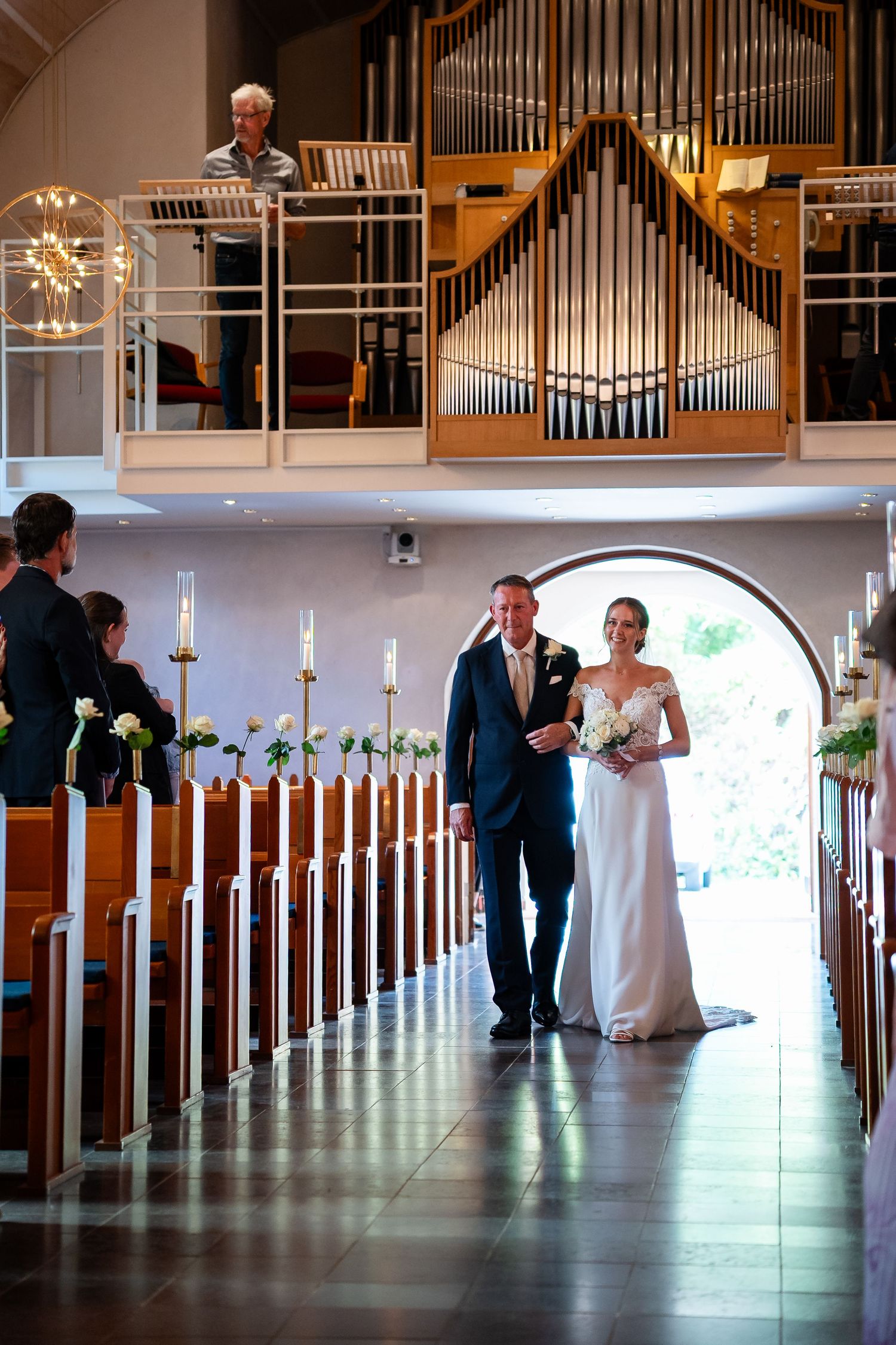 Bride and groom walking down church aisle with pipe organ backdrop during elegant wedding ceremony.