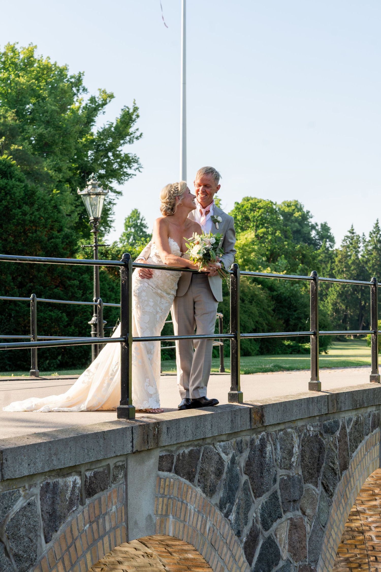 Bride and groom share a romantic moment on a stone bridge surrounded by lush greenery on their wedding day.