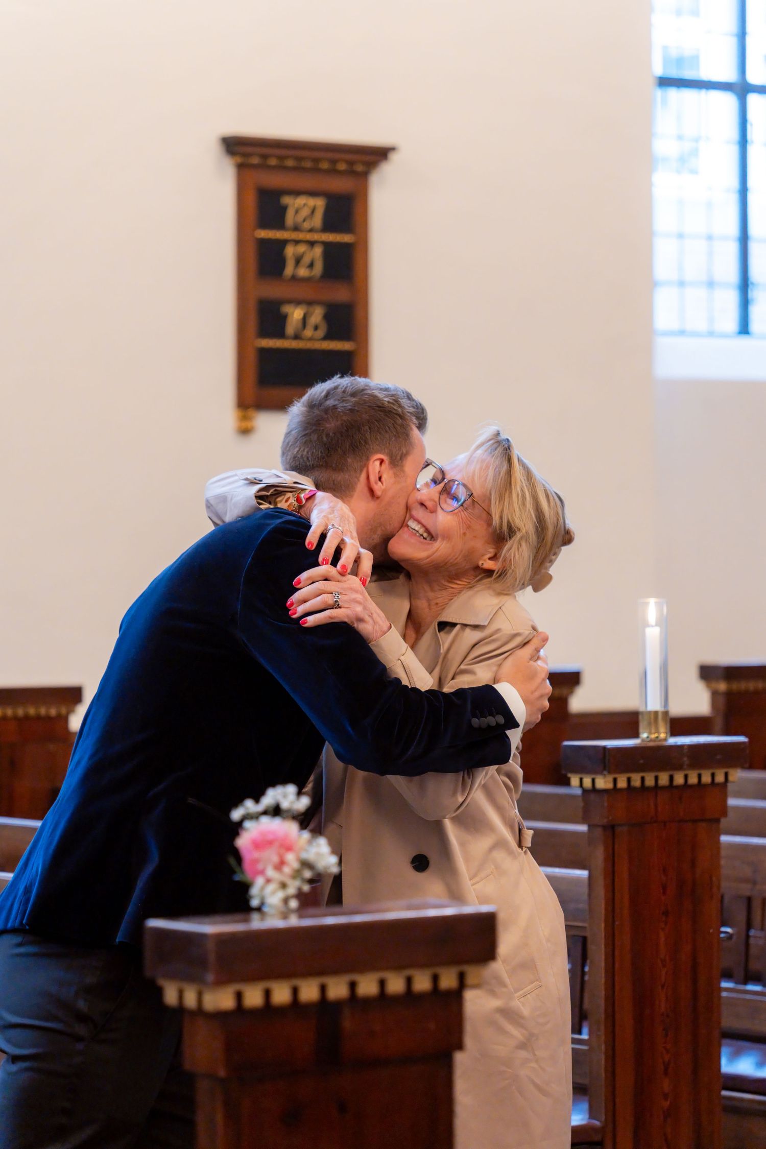 A couple embracing and kissing in a church setting with a wooden altar and shelves in the background.