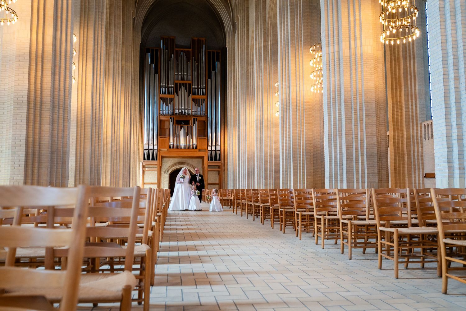 Bride and groom standing at the altar of a grand church with tall columns, wooden pews, and a large pipe organ.