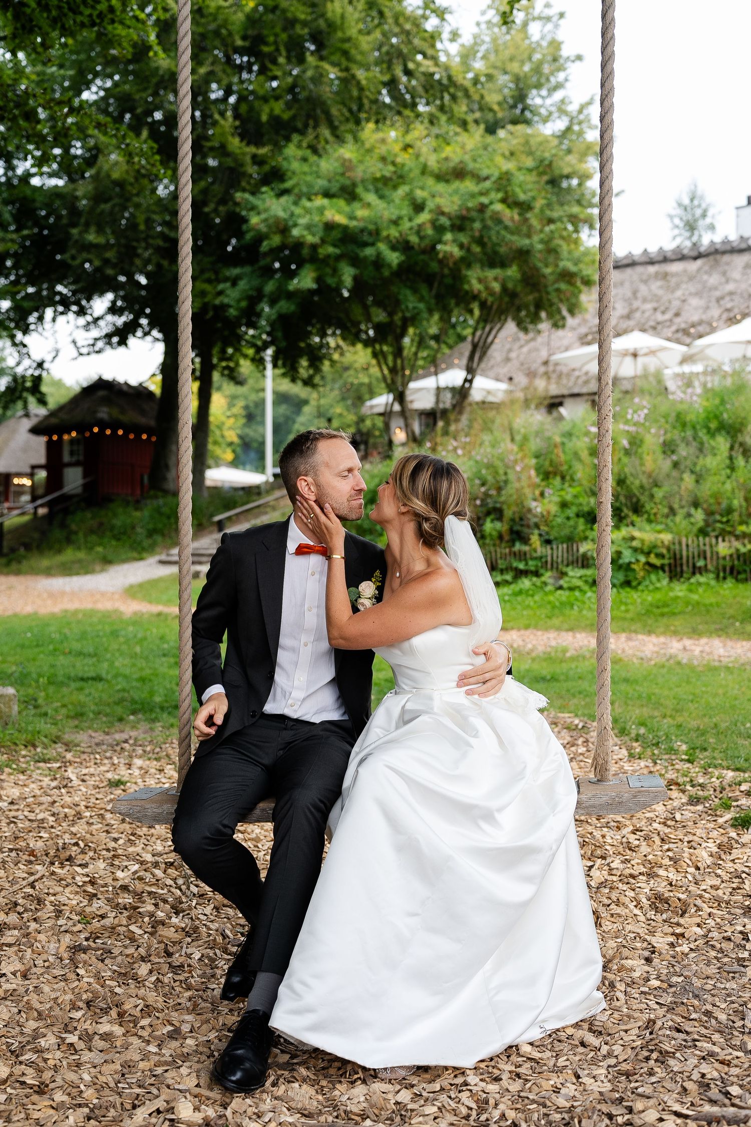 Bride and groom share a romantic moment on a rope swing outdoors, surrounded by lush greenery on their wedding day.