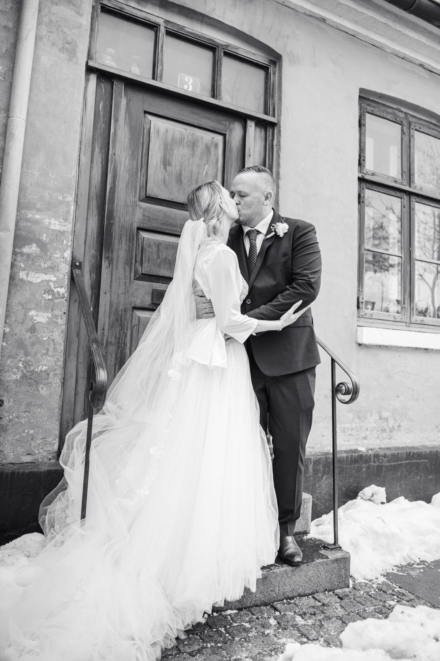 Black and white wedding photos on snowy steps outside historic building.