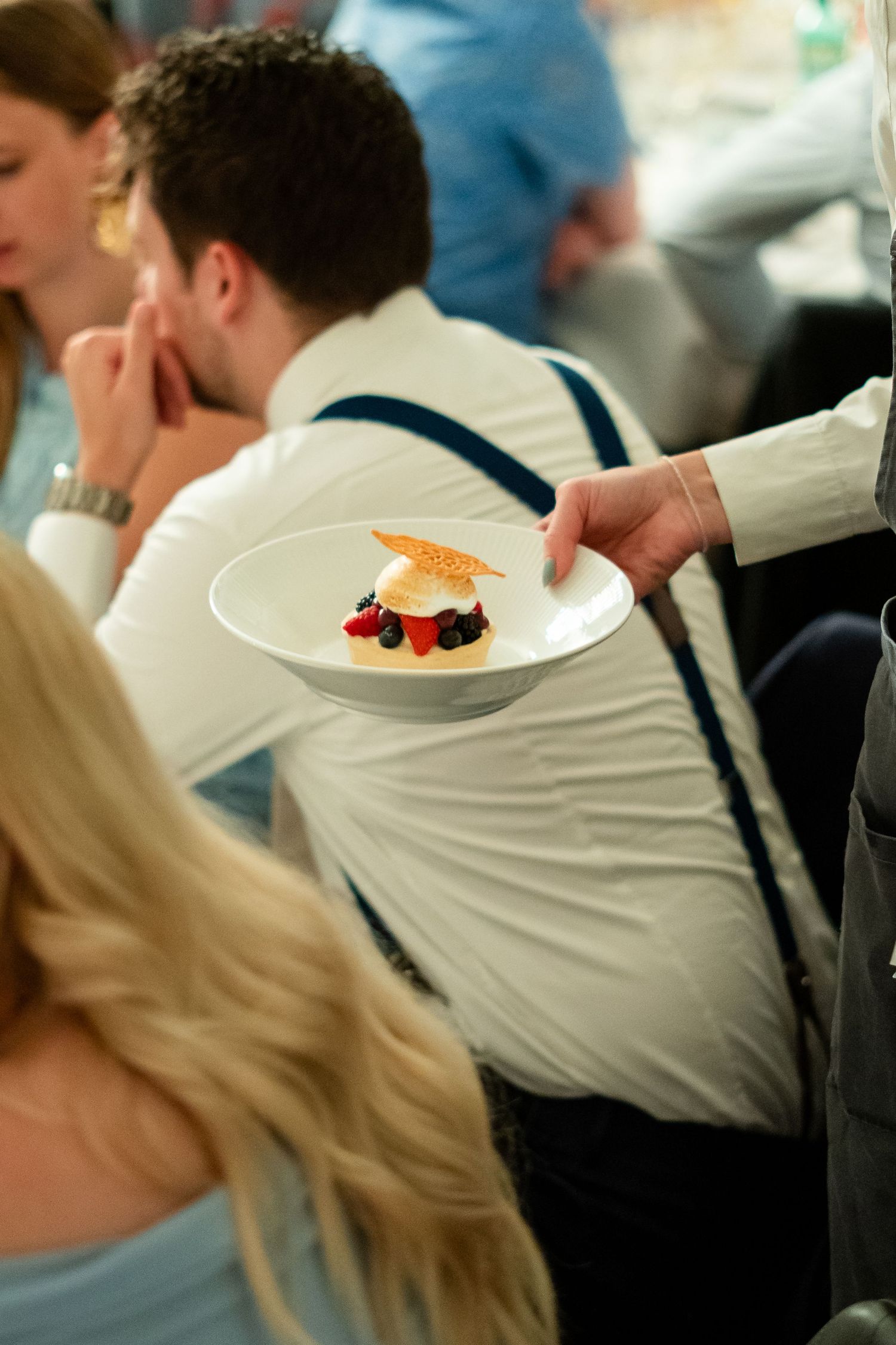 Waiter serving an elegant dessert with berries and caramel decoration on white plate at formal dining event.