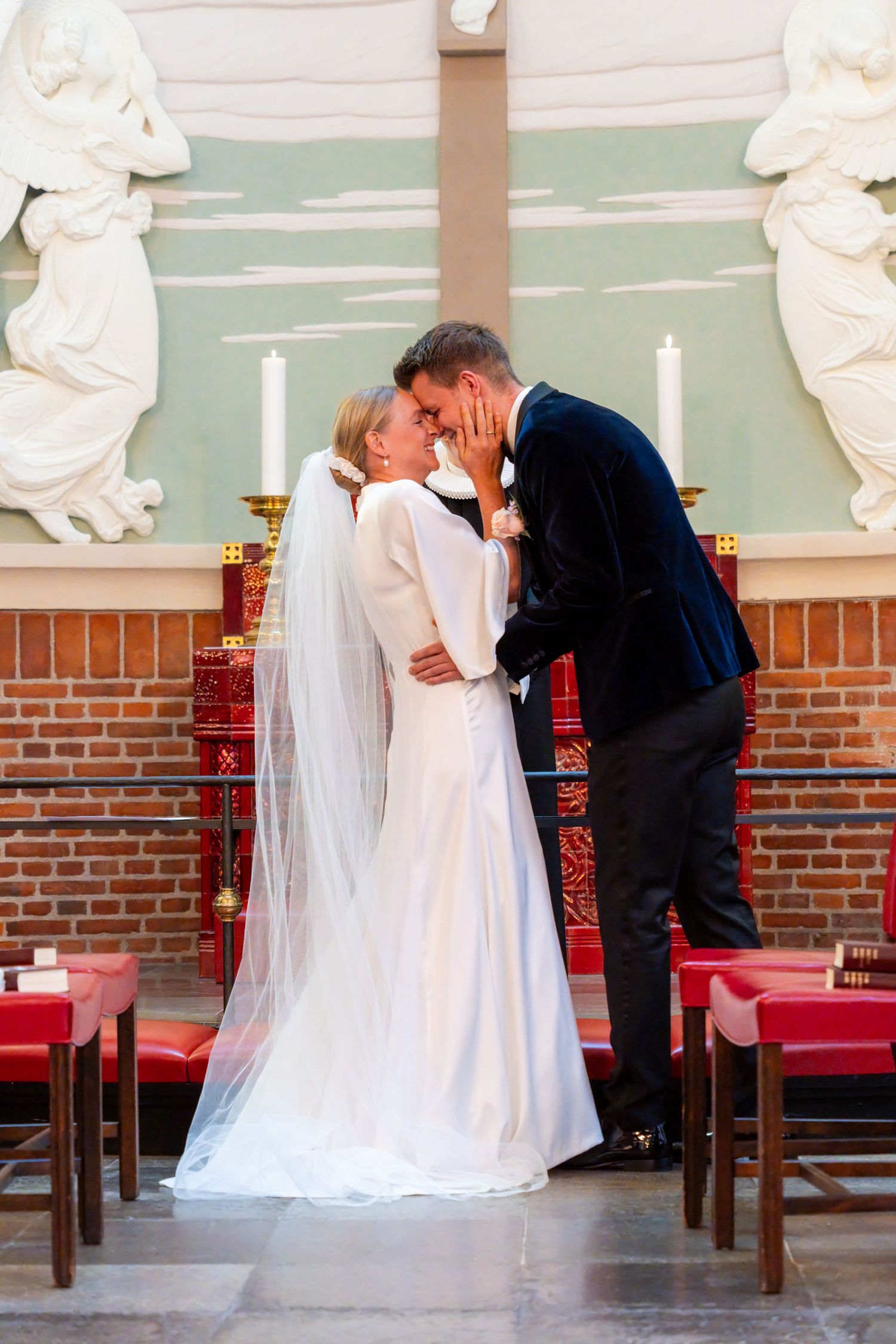 A bride and groom embrace tenderly in a church setting, with ornate architectural details in the background.