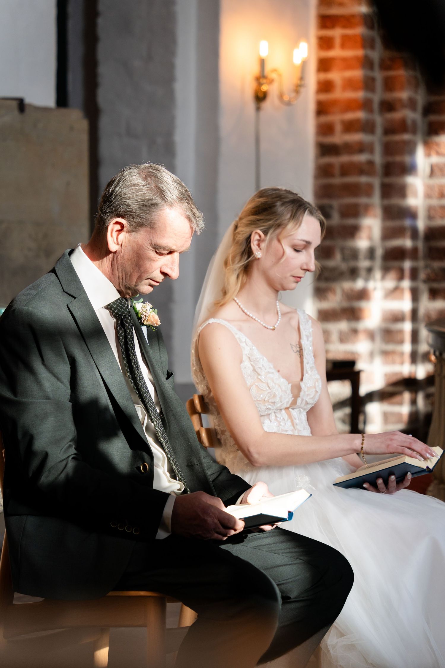 Wedding couple sitting and reading together in a brick-walled venue.