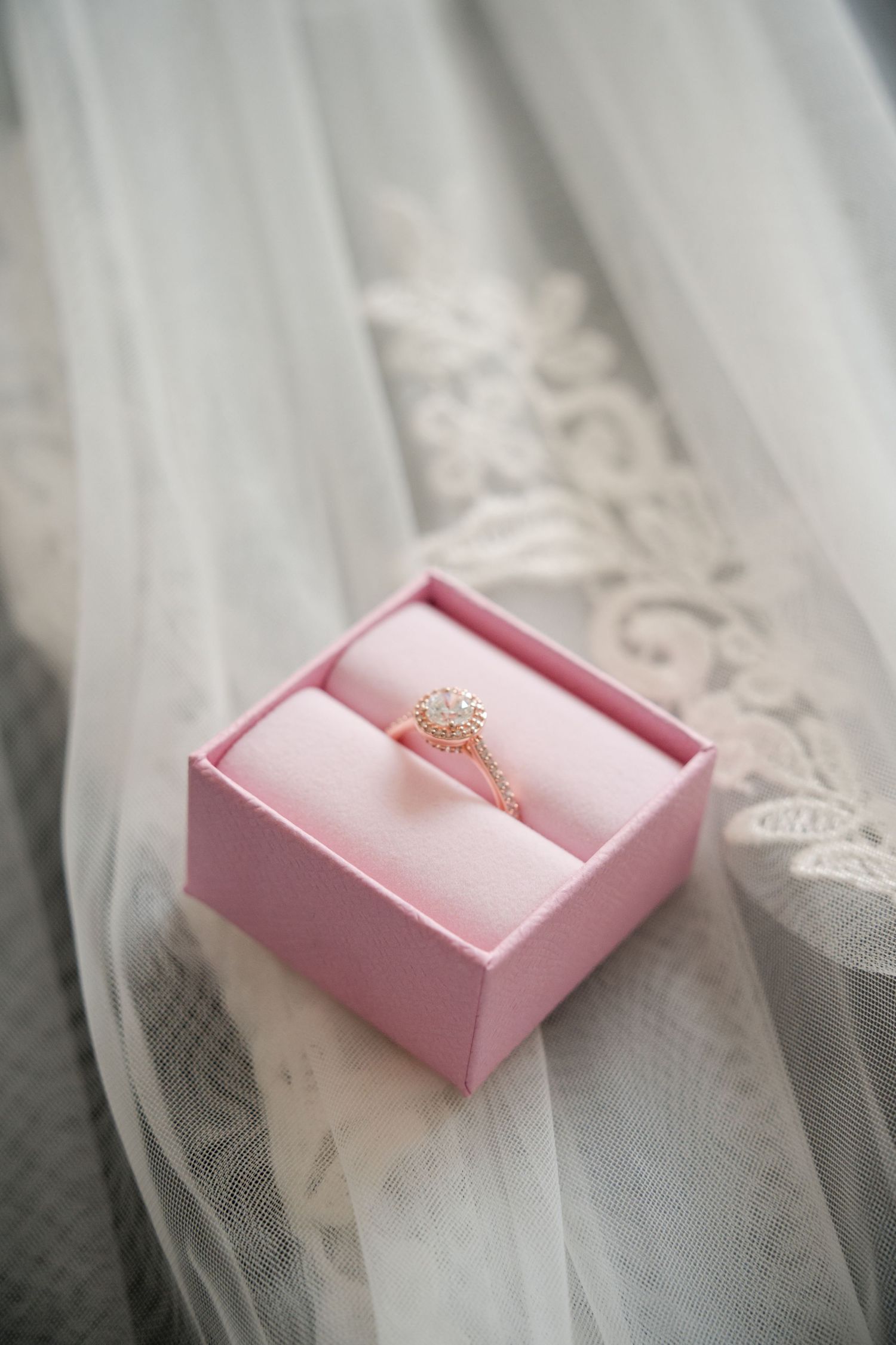 Delicate engagement ring displayed in a pink jewelry box on white tulle fabric.