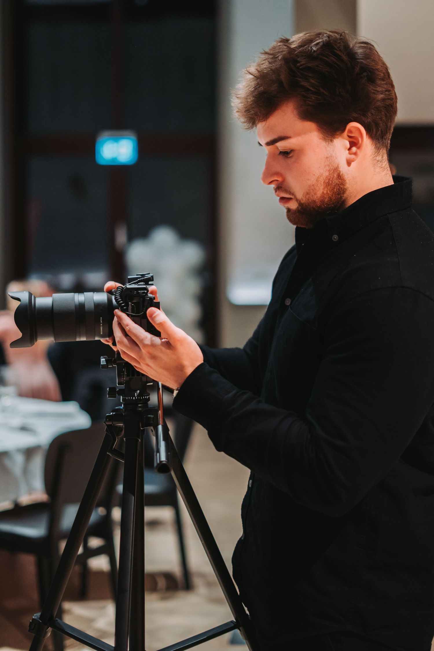 Photographer in dark clothing working with professional camera on tripod.