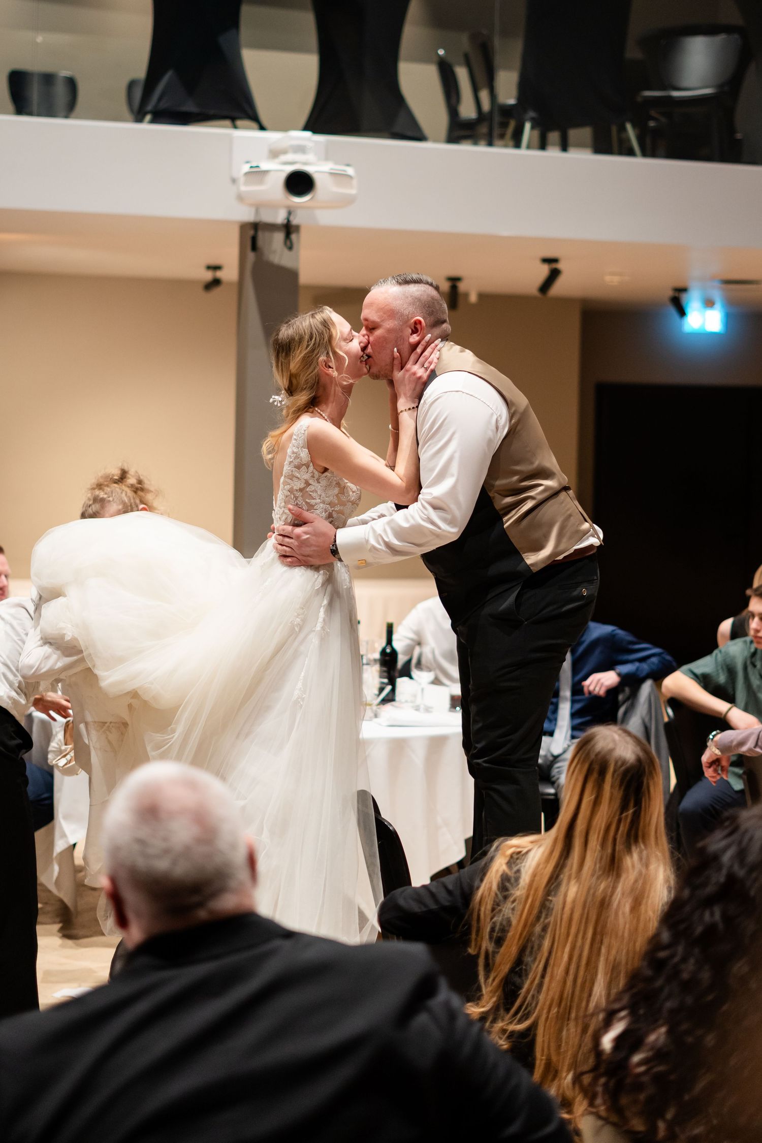 Bride and groom share a romantic first dance kiss at their wedding reception surrounded by seated guests.