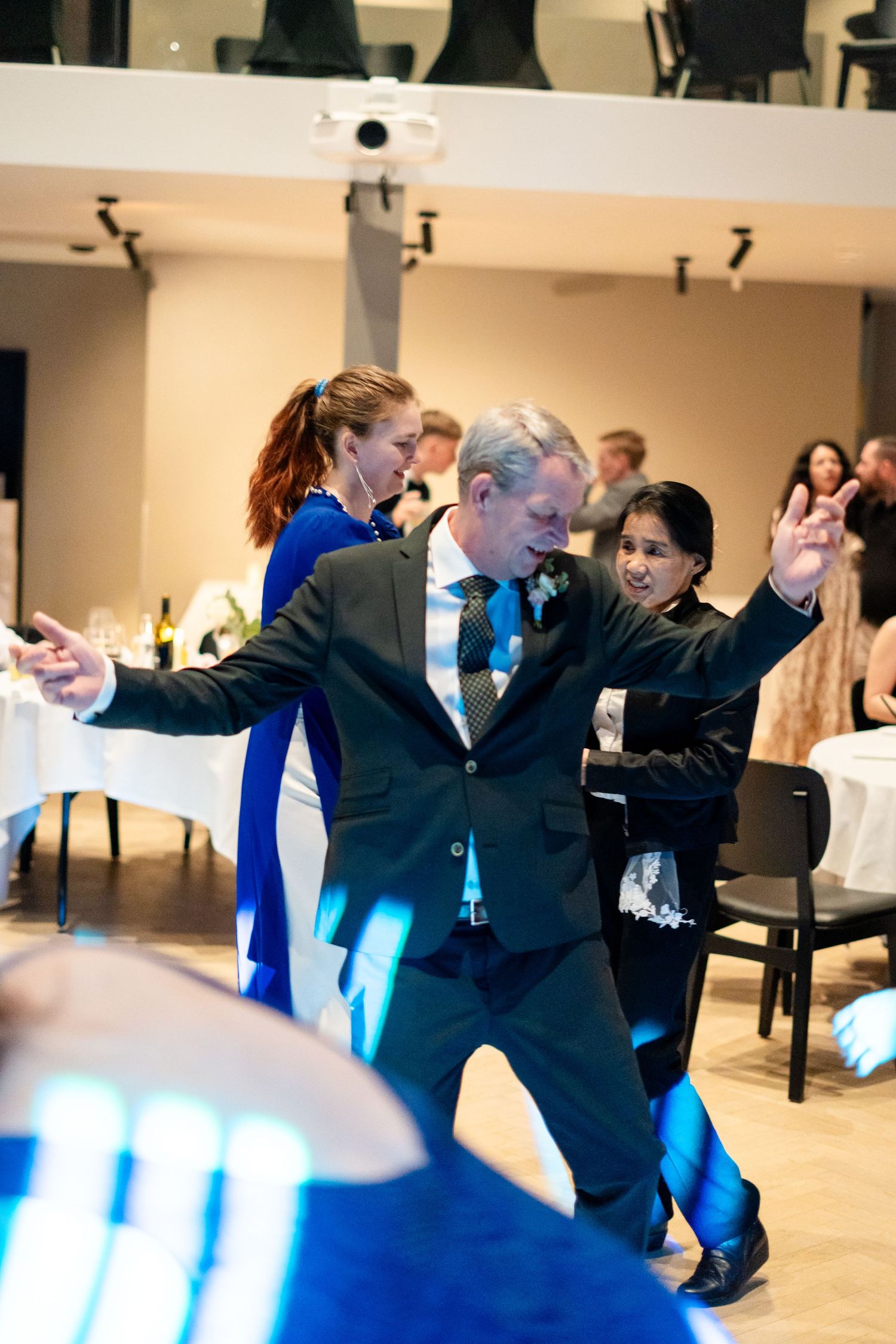Man in suit dancing energetically at a formal event, surrounded by guests and blue lighting on the dance floor.