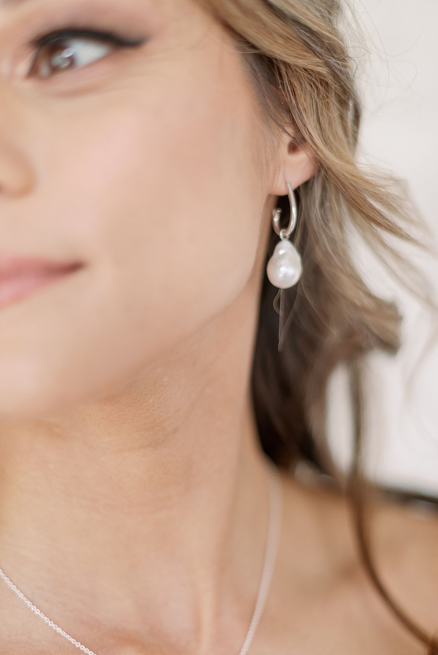 Elegant pearl drop earring worn with a delicate silver necklace.