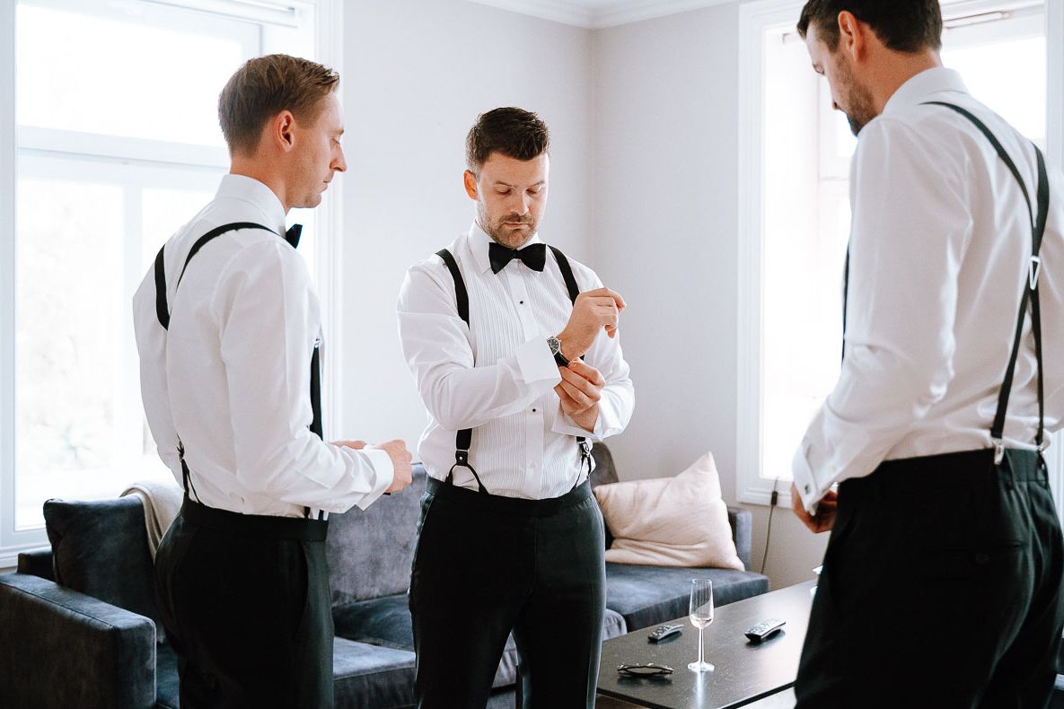 Groomsmen in white shirts and suspenders preparing for wedding ceremony.