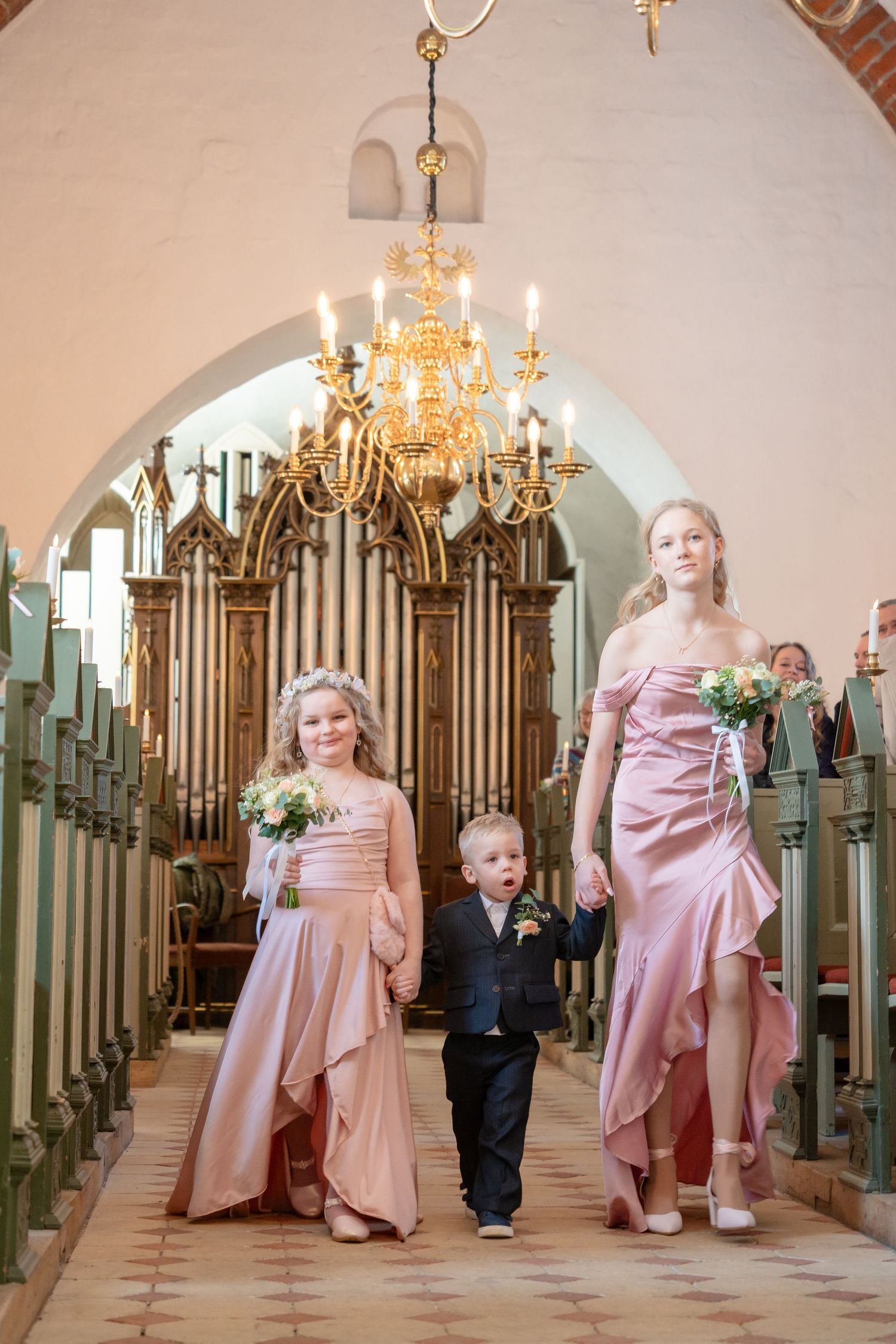 Wedding party in pink dresses standing near ornate church organ pipes.