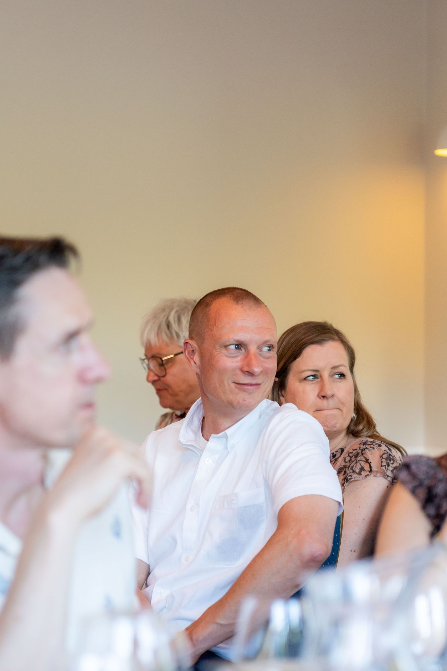 Group of adults sitting attentively at a meeting or conference, man in white polo shirt in focus.