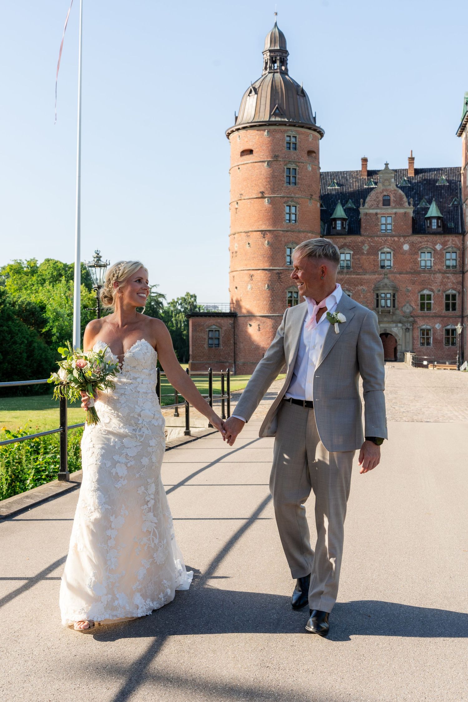 Bride and groom holding hands walking in front of a historic brick castle on their wedding day.