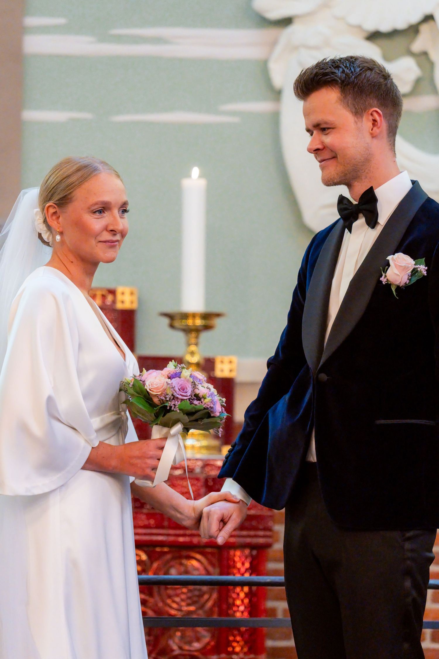 A bride and groom stand together at an altar, the bride holding a bouquet of flowers.