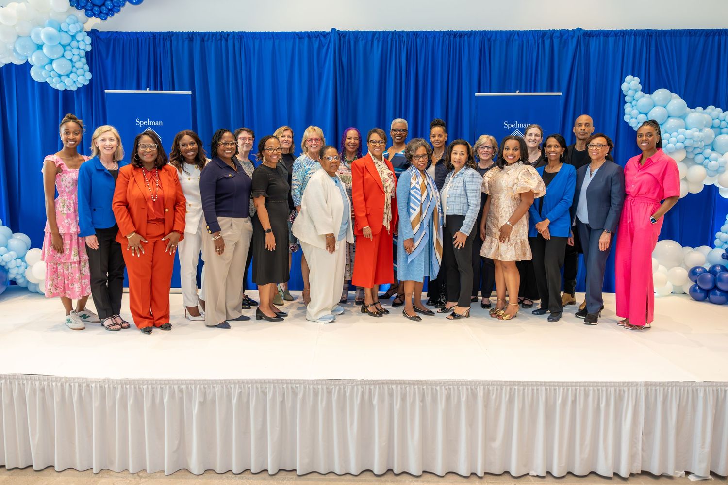 Large group photo with blue backdrop and decorative balloons at a formal event.