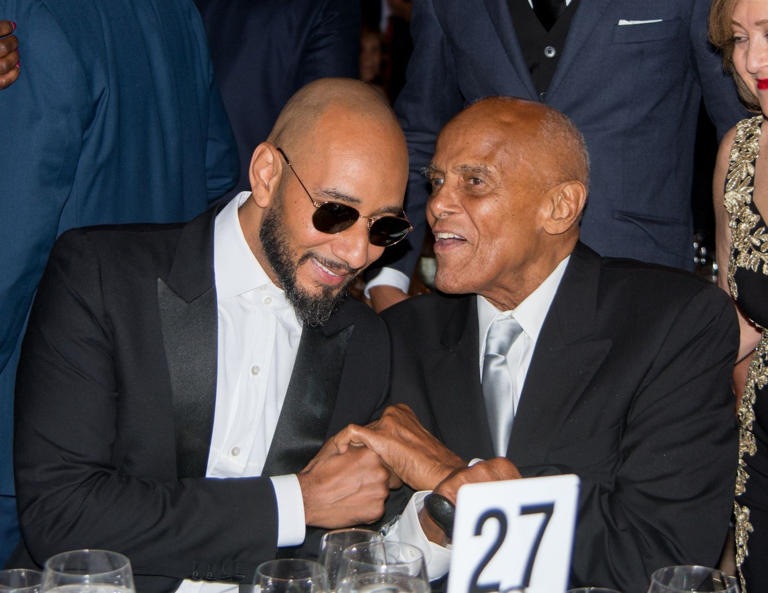 Two people in formal attire share a laugh while seated at what appears to be an awards show or gala event.